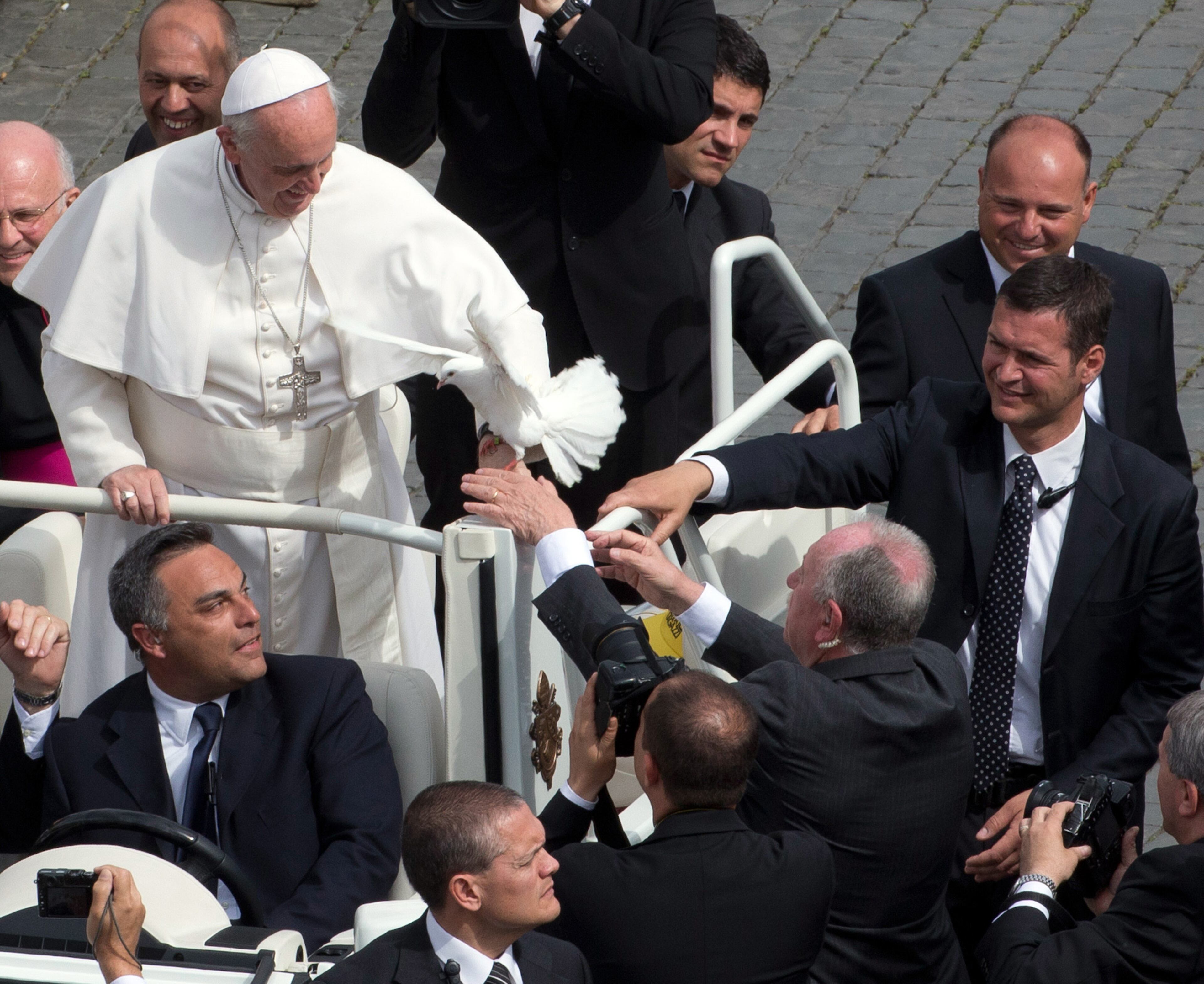 Security personnel try to take a dove grasping onto Pope Francis' hand during his weekly general audience in St. Peter Square at the Vatican, Wednesday, May 15, 2013. As Francis toured the square in his open-topped popemobile at his Wednesday audience with the public, someone at the edge of the crowd thrust a white bird cage at him. Looking puzzled, his security detail took the cage, containing a pair of white doves, and handed it to Francis. Without hesitation, the pope opened the cage door, thrust a hand inside and extracted one dove, and with a flick of his hand, sent the bird flying over the square. (AP Photo/Alessandra Tarantino)