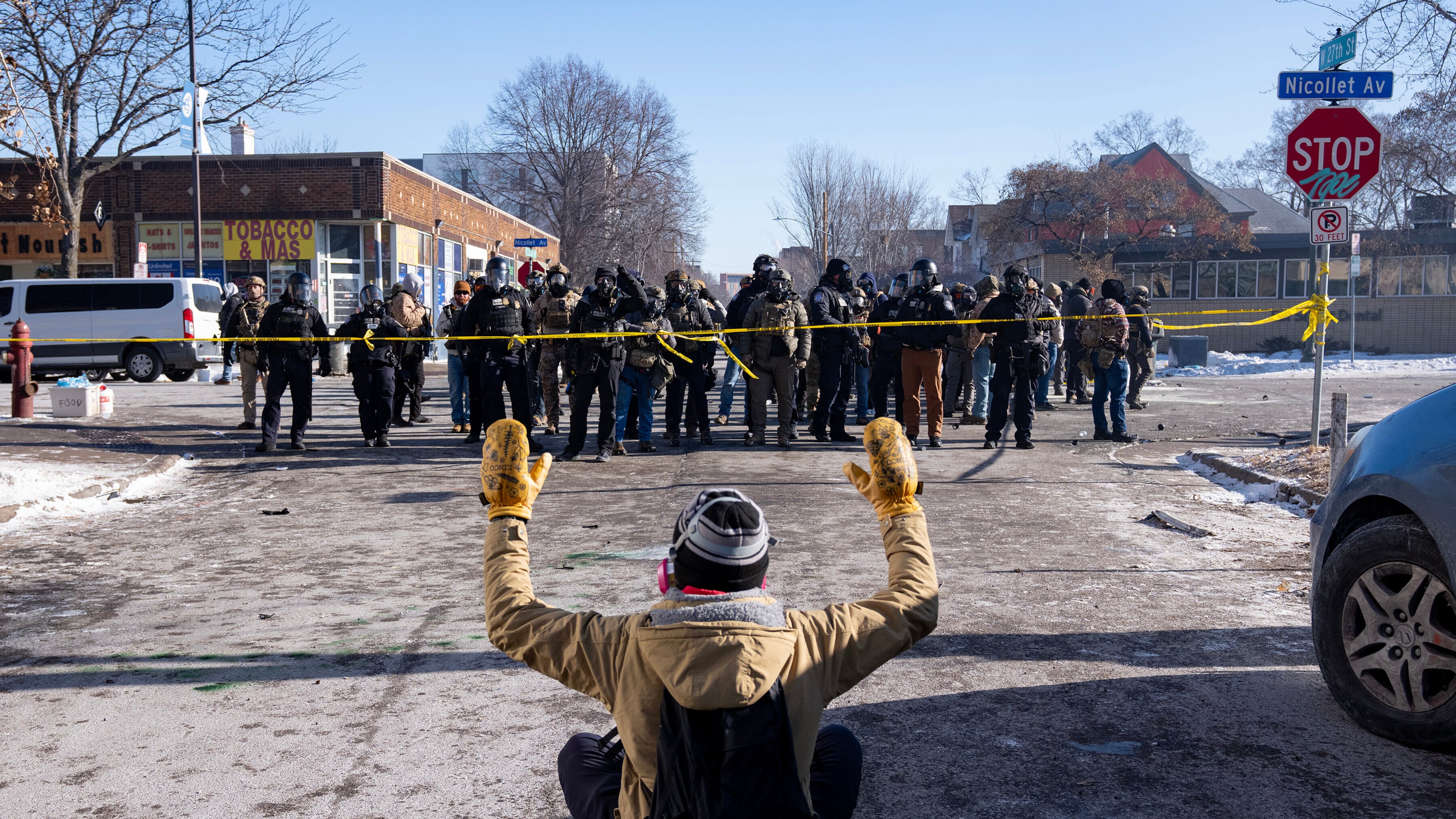 A protester sits on the street with his arms up in front of federal agents in Minneapolis, on Saturday, Jan. 24, 2026. (Alex Kormann/Star Tribune via AP)