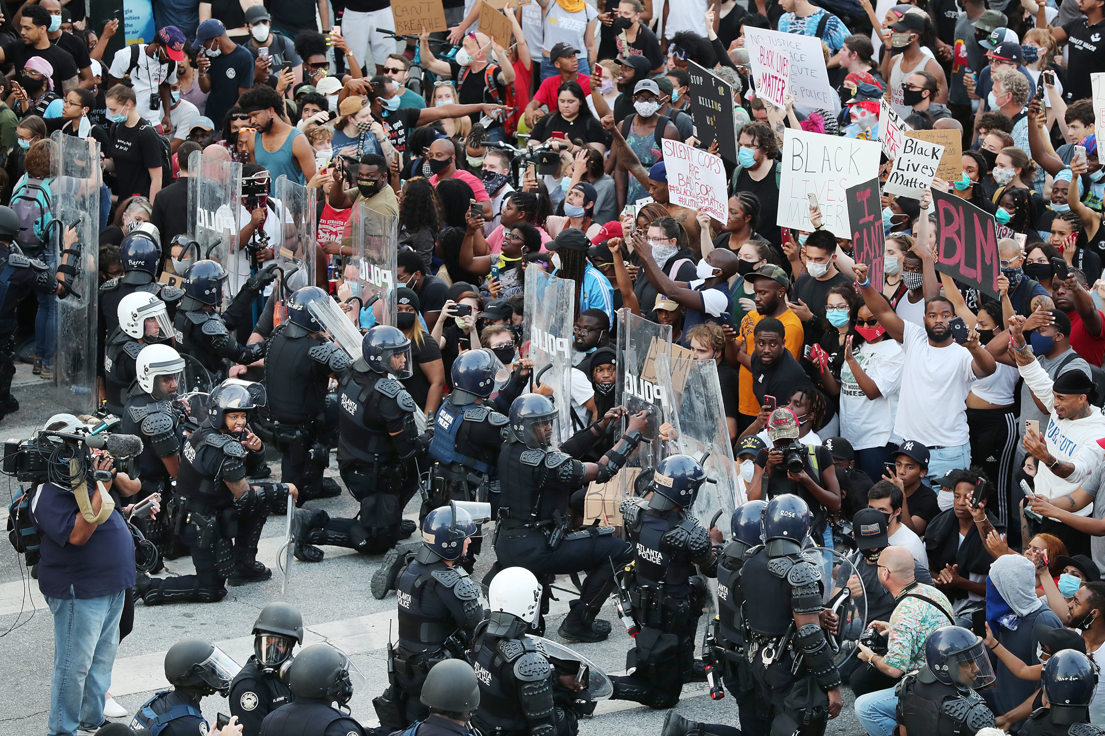 In a show of peace and solidarity, law enforcement officials with riot shields take a knee before protesters during a fourth day of protests on Monday, June 1, 2020, in Atlanta.