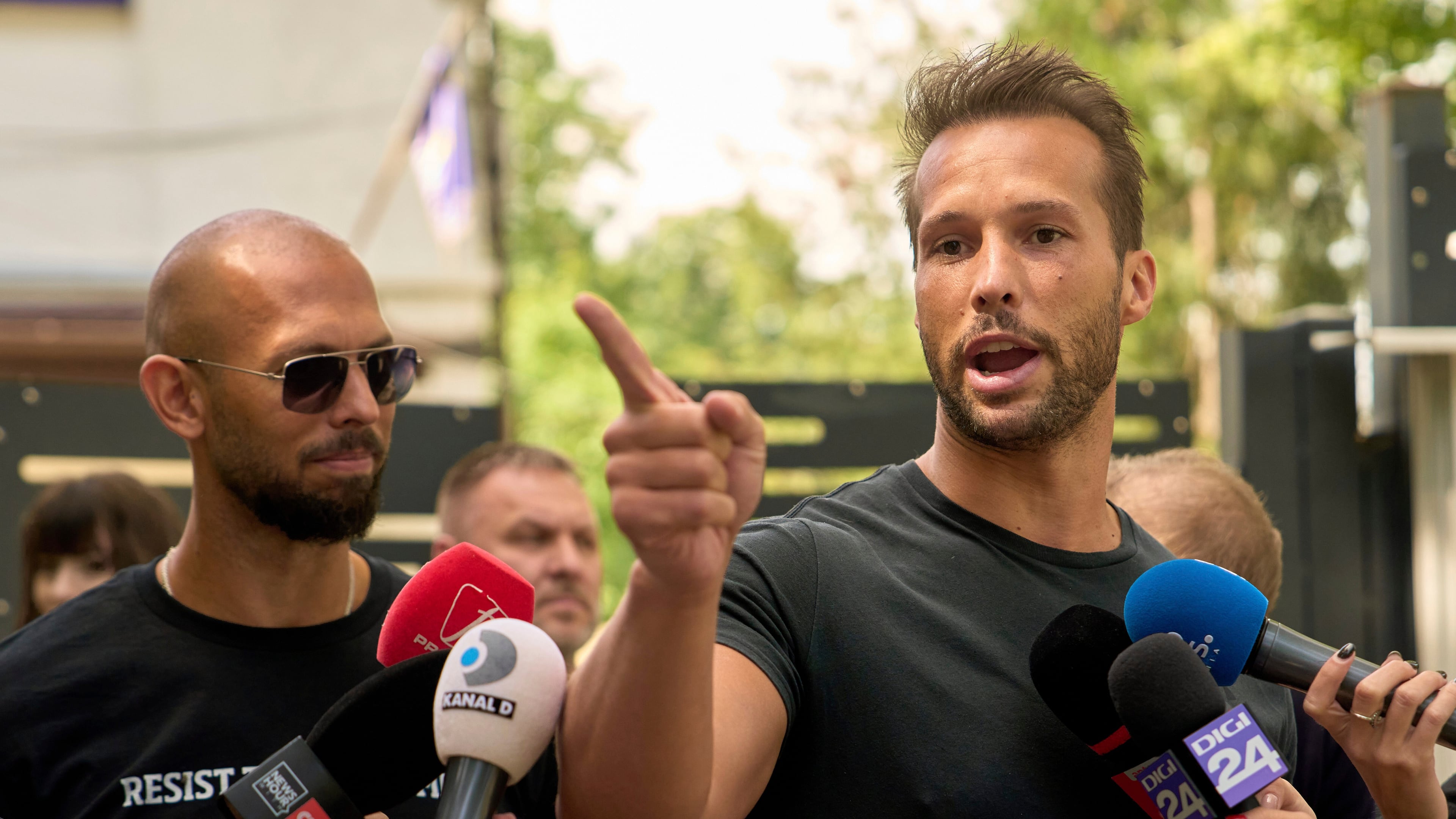 FILE - Andrew Tate, left, watches his brother Tristan speak, outside a police station in Voluntari, Romania, May 21, 2025. (AP Photo/Vadim Ghirda, File)