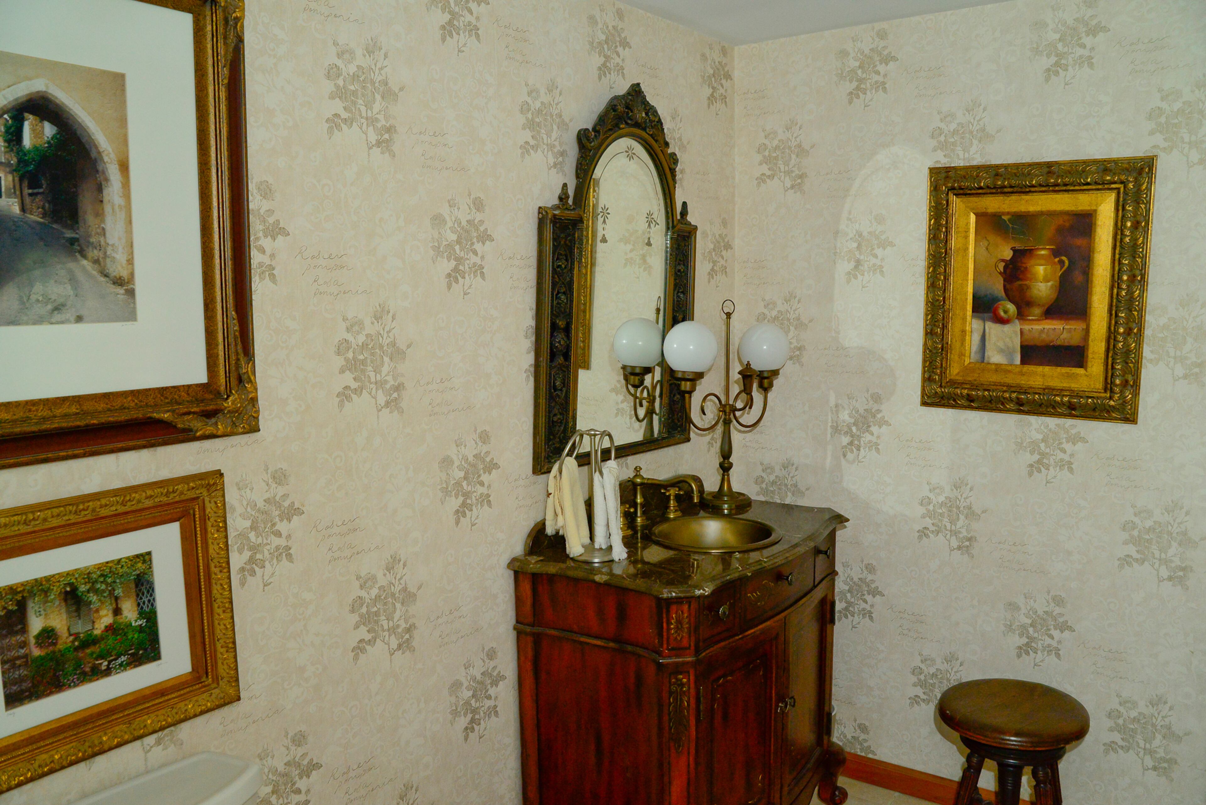 The powder room is dressed up with wallpaper, a furniture-like vanity and framed French scenes.