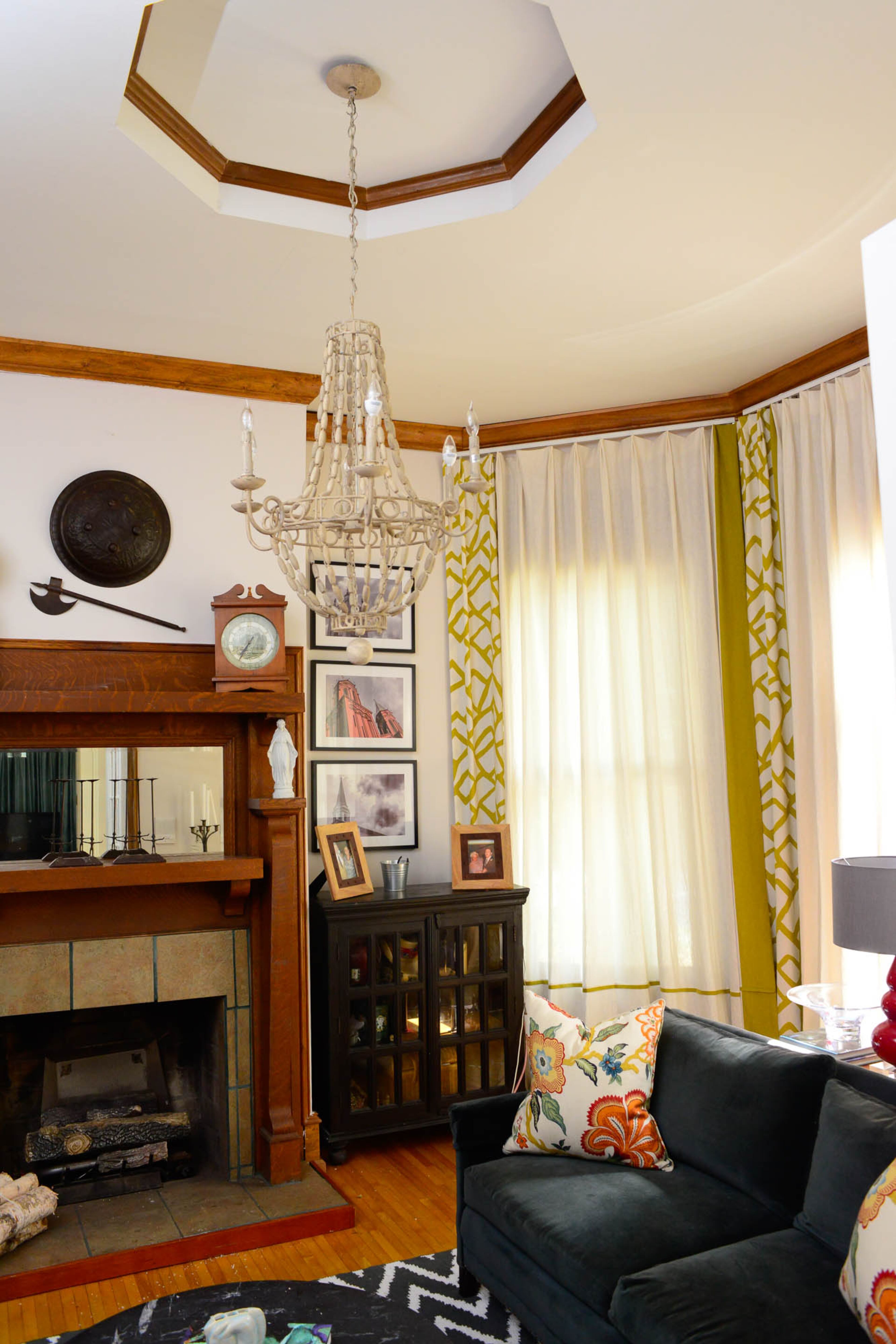 Troy Farina and John Ishmael use the twin parlors to either side of their hexagonal foyer as a living room and a TV room. In the living room, the light fixture, which Ishmael found 15 years ago at a yard sale, and floor-to-ceiling curtains work together to emphasize the room’s height and ceiling detail.