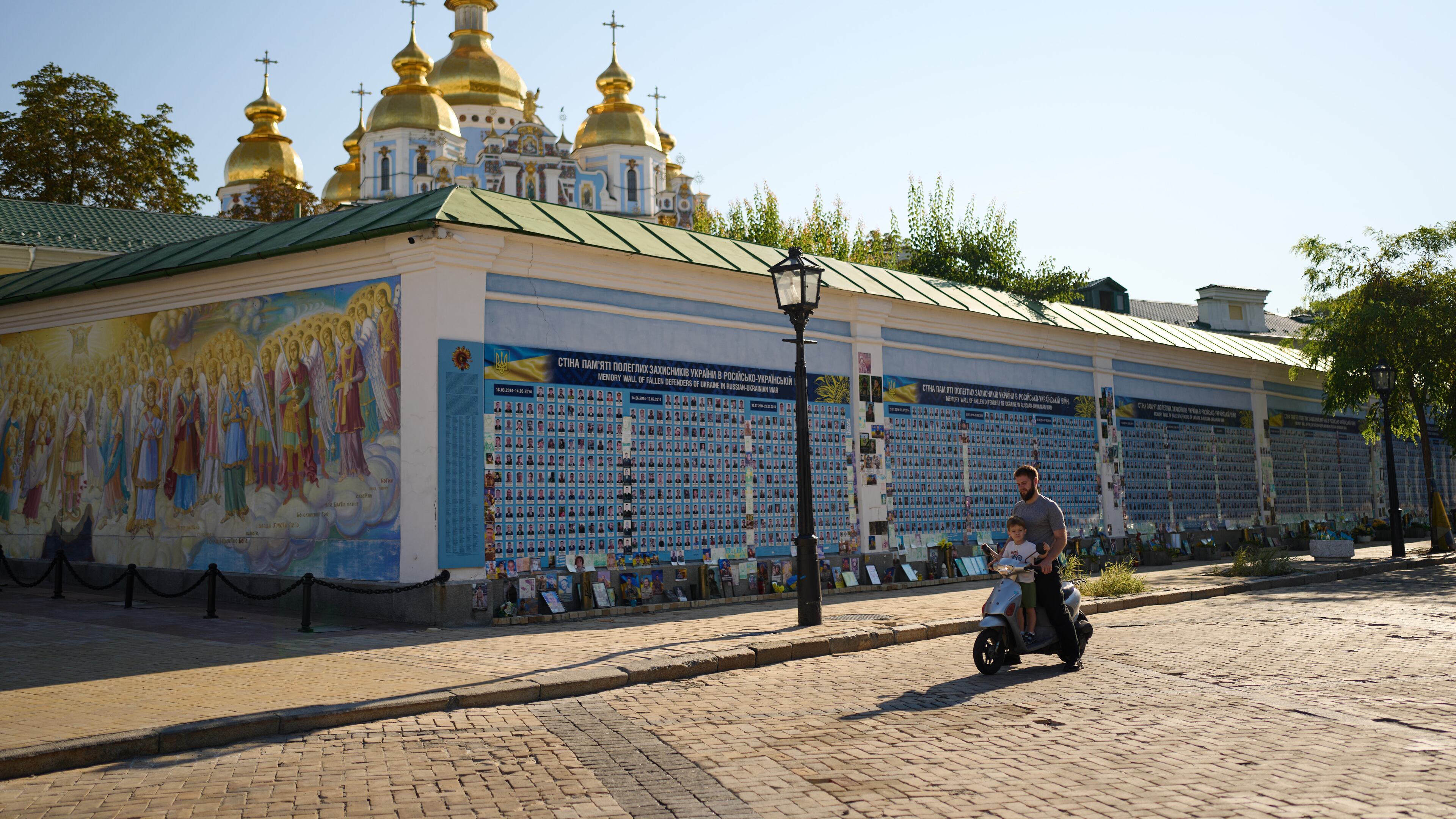 A man and a child observe a daily nationwide minute of silence in memory of soldiers killed in the war with Russia next to The Wall of Remembrance of the Fallen for Ukraine in Kyiv, Friday, Aug. 21, 2026. (AP Photo/Francisco Seco)