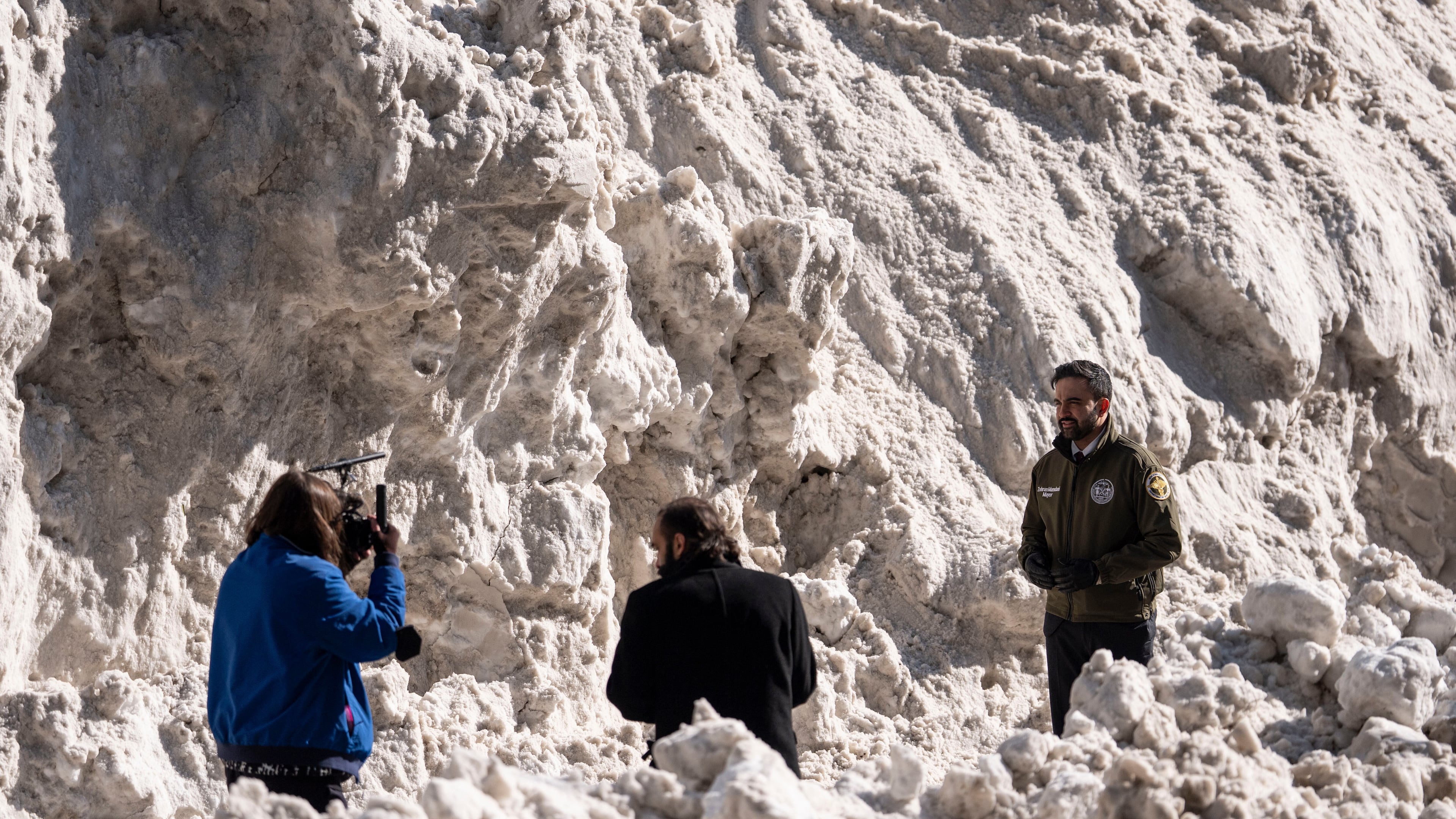New York City Mayor Zohran Mamdani, right, stands backdropped by a pile of snow while recording a video during a visit to the Department of Sanitation's snow melting operations in New York, Thursday, Jan. 29, 2026. (AP Photo/Yuki Iwamura)