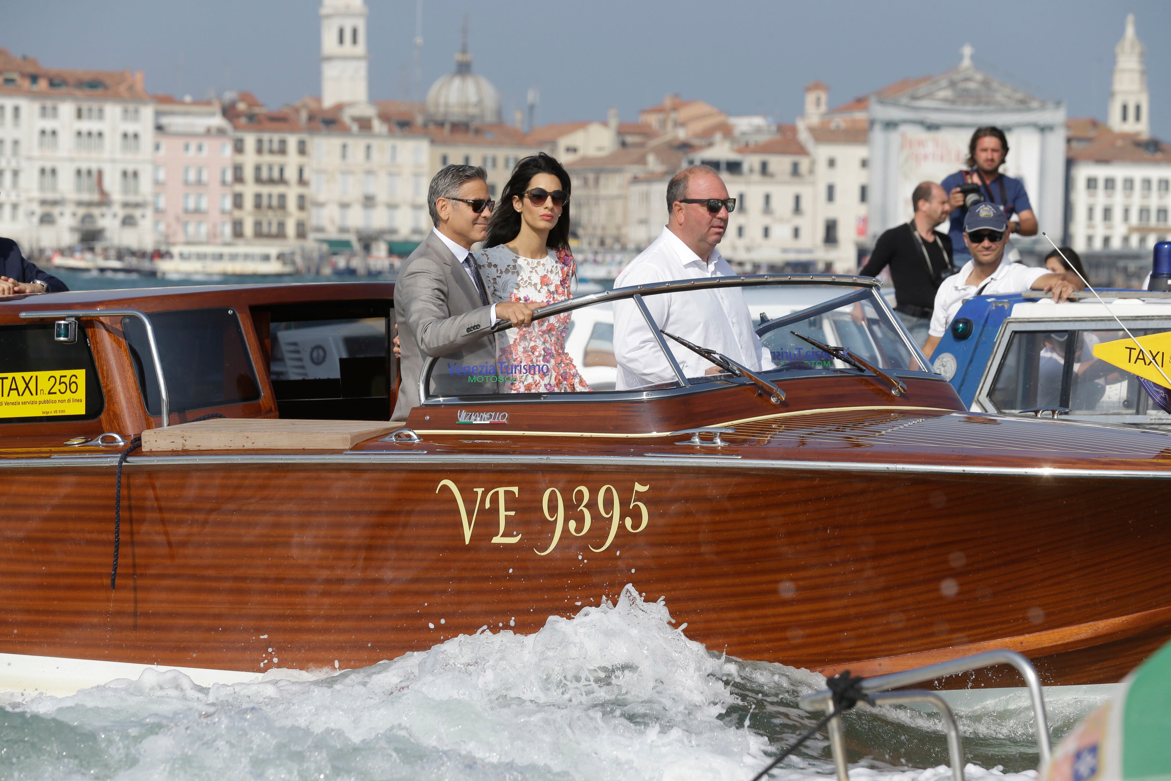 George Clooney is flanked by his wife Amal Alamuddin as they cruise the Grand Canal after leaving the Aman luxury Hotel in Venice, Italy, Sunday, Sept. 28, 2014. George Clooney married human rights lawyer Amal Alamuddin Saturday, the actor's representative said, out of sight of pursuing paparazzi and adoring crowds. (AP Photo/Luca Bruno)