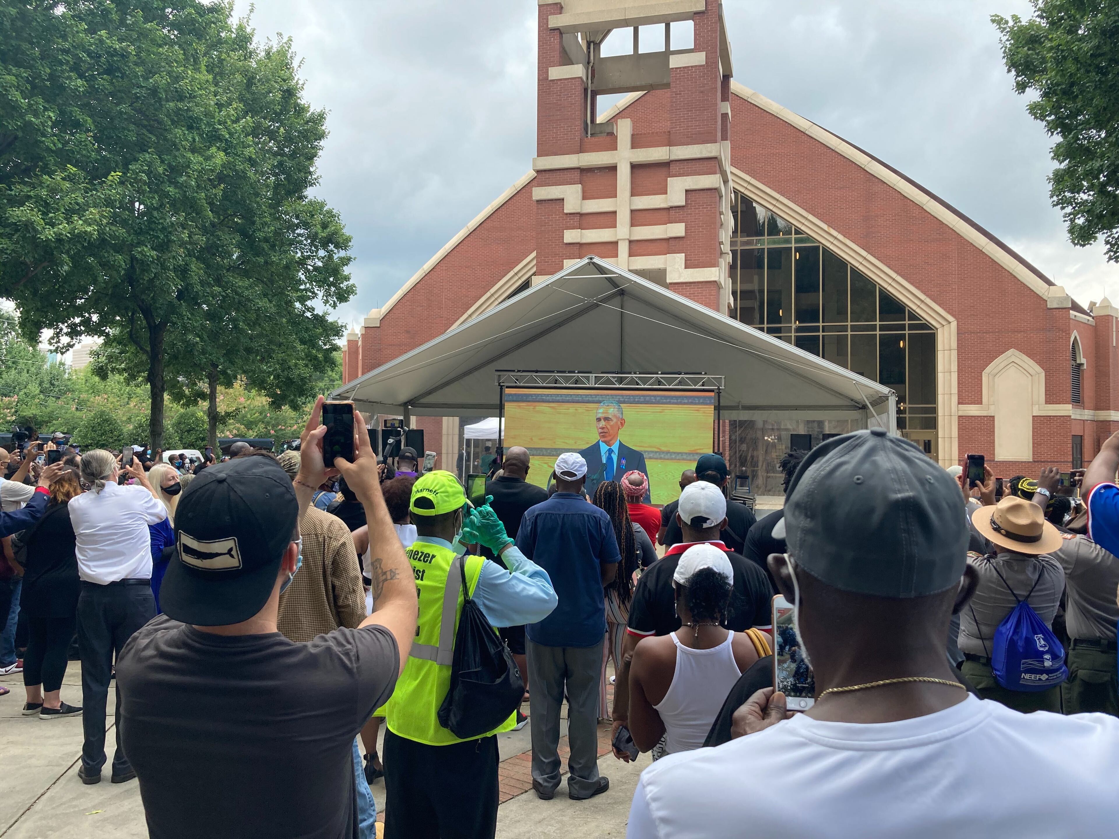 President Barack Obama is shown on a big screen outside Ebenezer Baptist Church as he gave the eulogy for Congressman John Lewis. An attentive crowd included many capturing the moment on their smaller screens. (J.D. Capelouto / AJC)