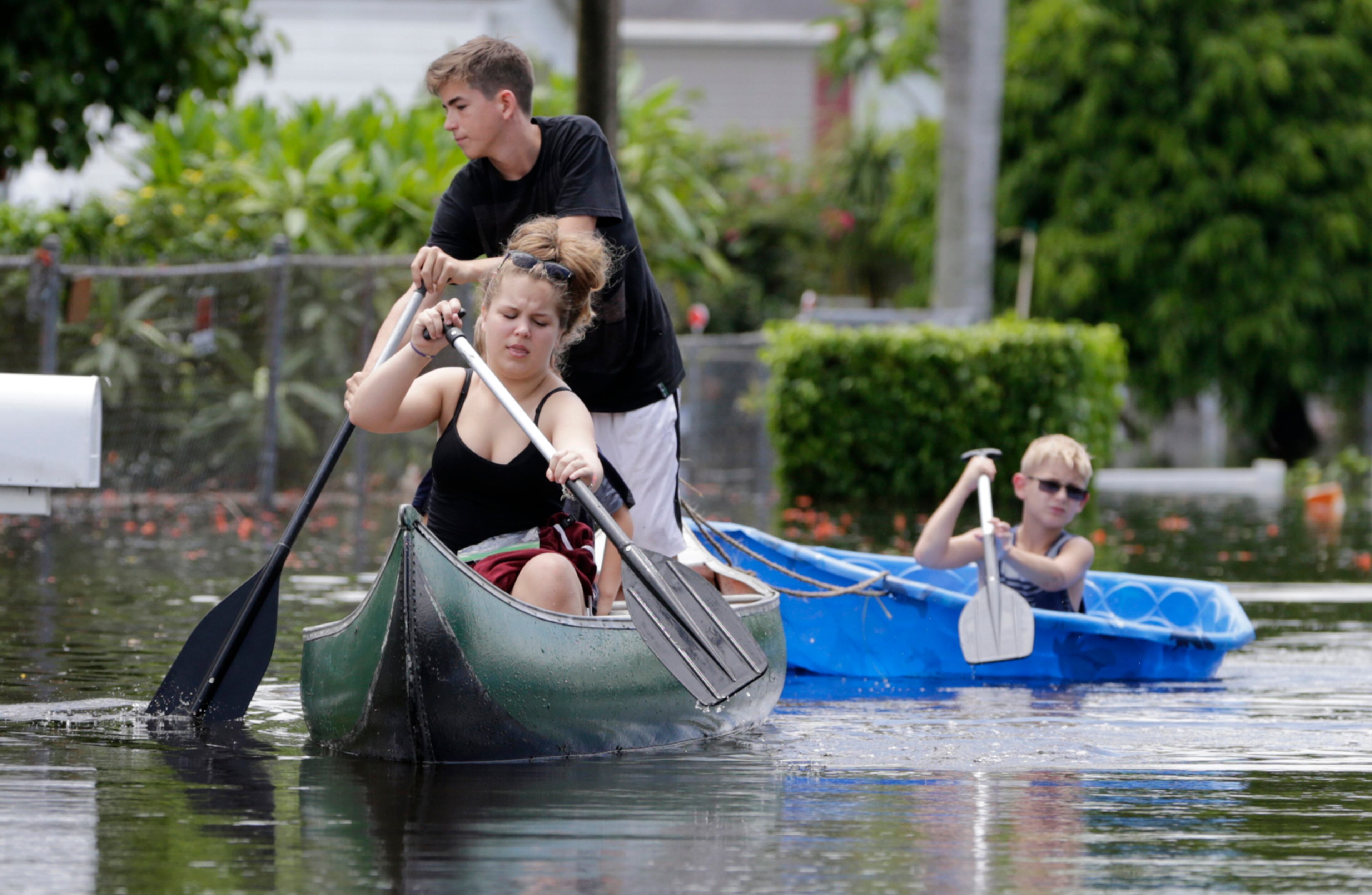 Isabella and Timothy, who did not want their last names used, navigate flooded streets following heavy rains, Wednesday, June 7, 2017, in Davie, Fla. Several South Florida cities set rainfall records as heavy rain continues to fall, bringing the potential for further flooding. Wallace put up the "Slow No Wake" sign to prevent fast moving vehicles from flooding her trailer. (AP Photo/Lynne Sladky)