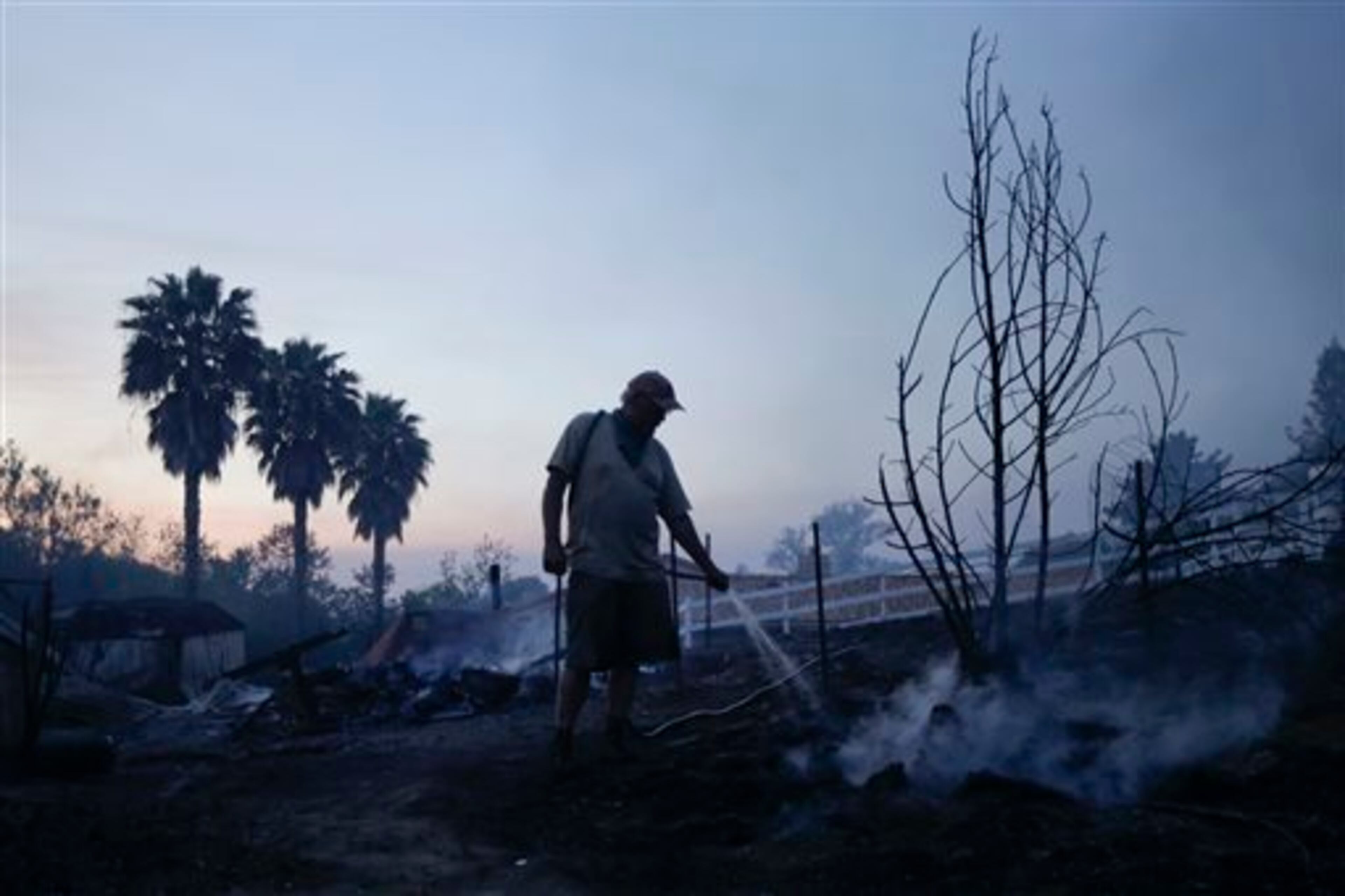 Jeff Buchanan waters the scorched earth around a neighbor's house that burned to the ground during a wildfire Thursday, May 15, 2014, in Escondido, Calif. One of the nine fires burning in San Diego County suddenly flared Thursday afternoon and burned close to homes, trigging thousands of new evacuation orders.(AP Photo/Gregory Bull)