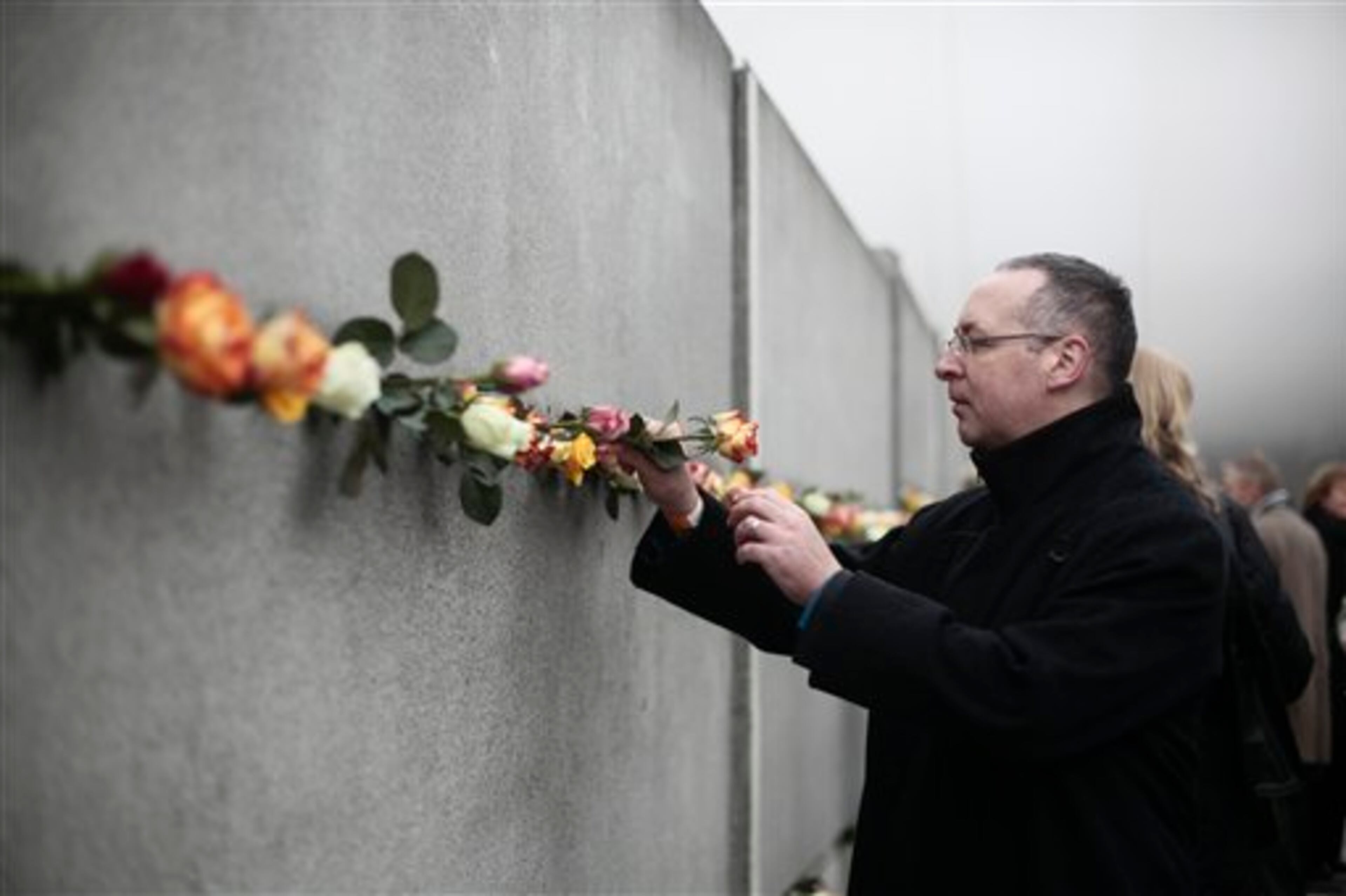 A man puts a flower in a crack of the former Berlin Wall to commemorate the victims of the wall at the Berlin Wall memorial site at Bernauer Strasse in Berlin, Germany, Sunday, Nov. 9, 2014. 25 years ago - on Nov. 9, 1989 - the East-German government lifted travel restrictions and thousands of East Berliners had pushed their way past perplexed border guards to celebrate freedom with their brethren in the West. (AP Photo/Markus Schreiber)