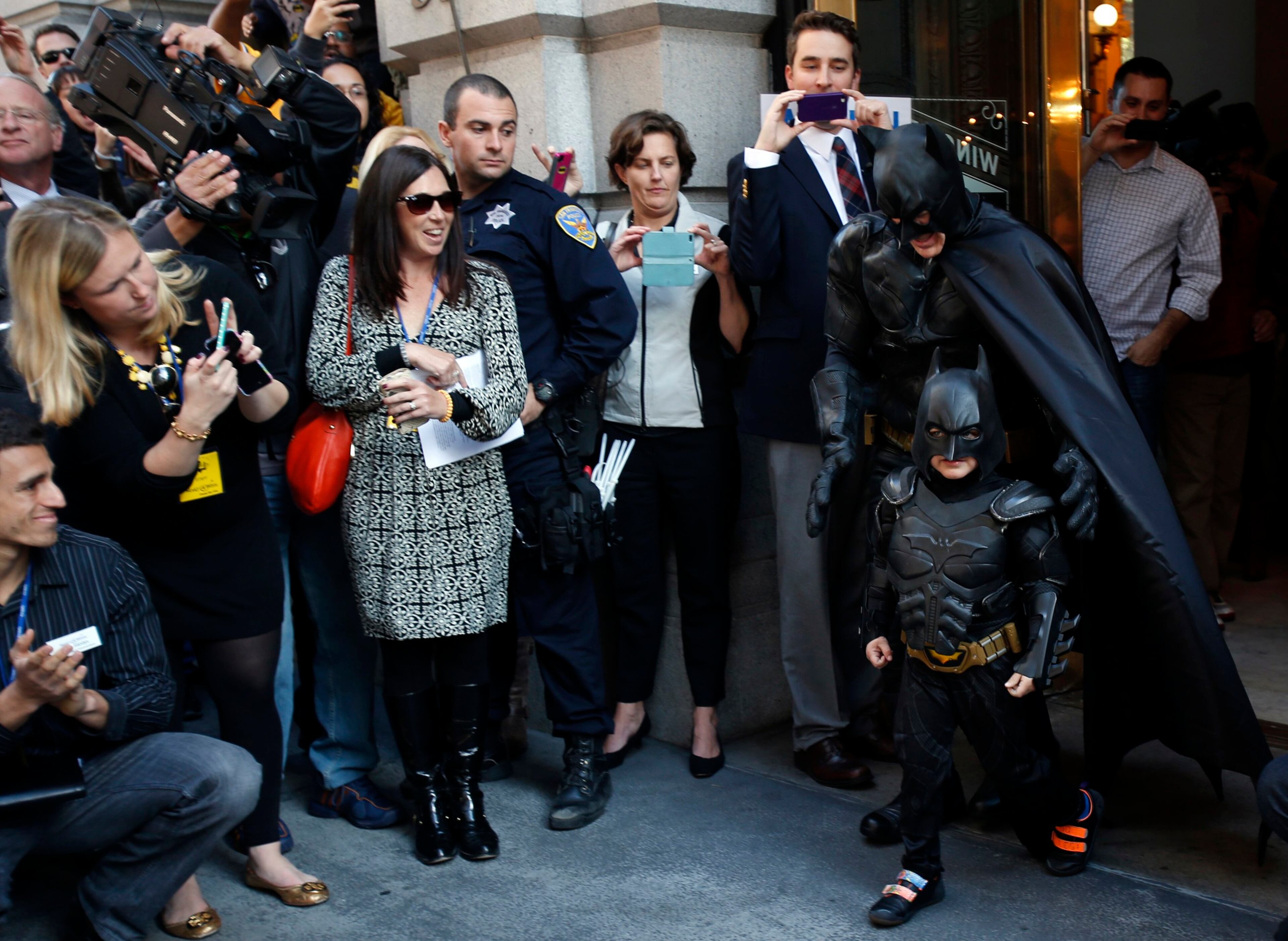 Five-year-old leukemia survivor Miles dressed as "Batkid" and a man dressed as Batman leave a bank after they apprehended "The Riddler" as part of a day arranged by the Make-A-Wish Foundation in San Francisco, California November 15, 2013. The young cancer survivor will be treated to various super hero scenarios including receiving a commendation at San Francisco City Hall.