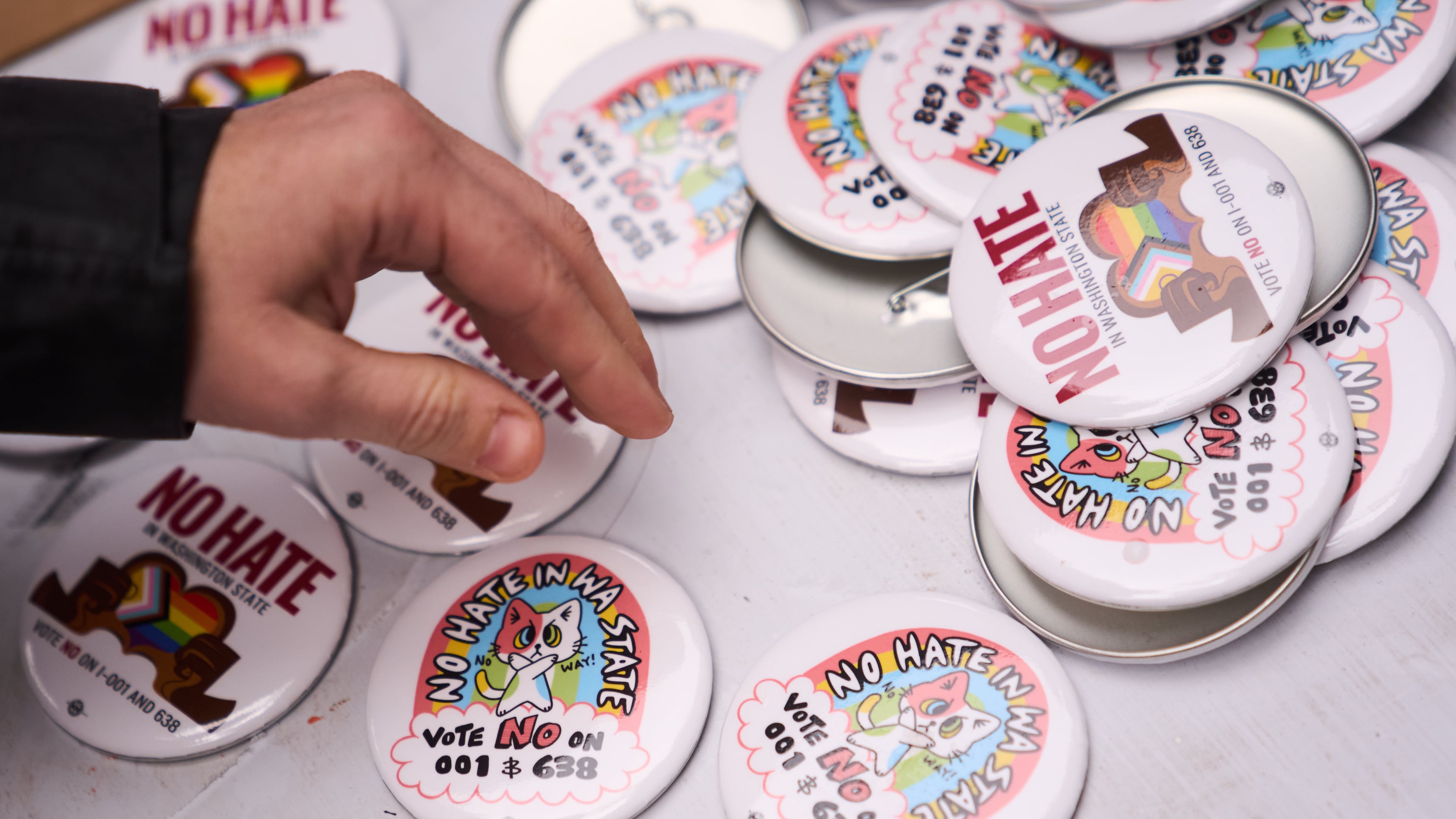 A person picks up a button during a "No Hate in WA State" rally against multiple initiatives on the November ballot, including Washington State Initiative 638, which would prohibit transgender girls from competing in girls' sports, Saturday, Oct. 17, 2026, in Seattle. (AP Photo/Lindsey Wasson)