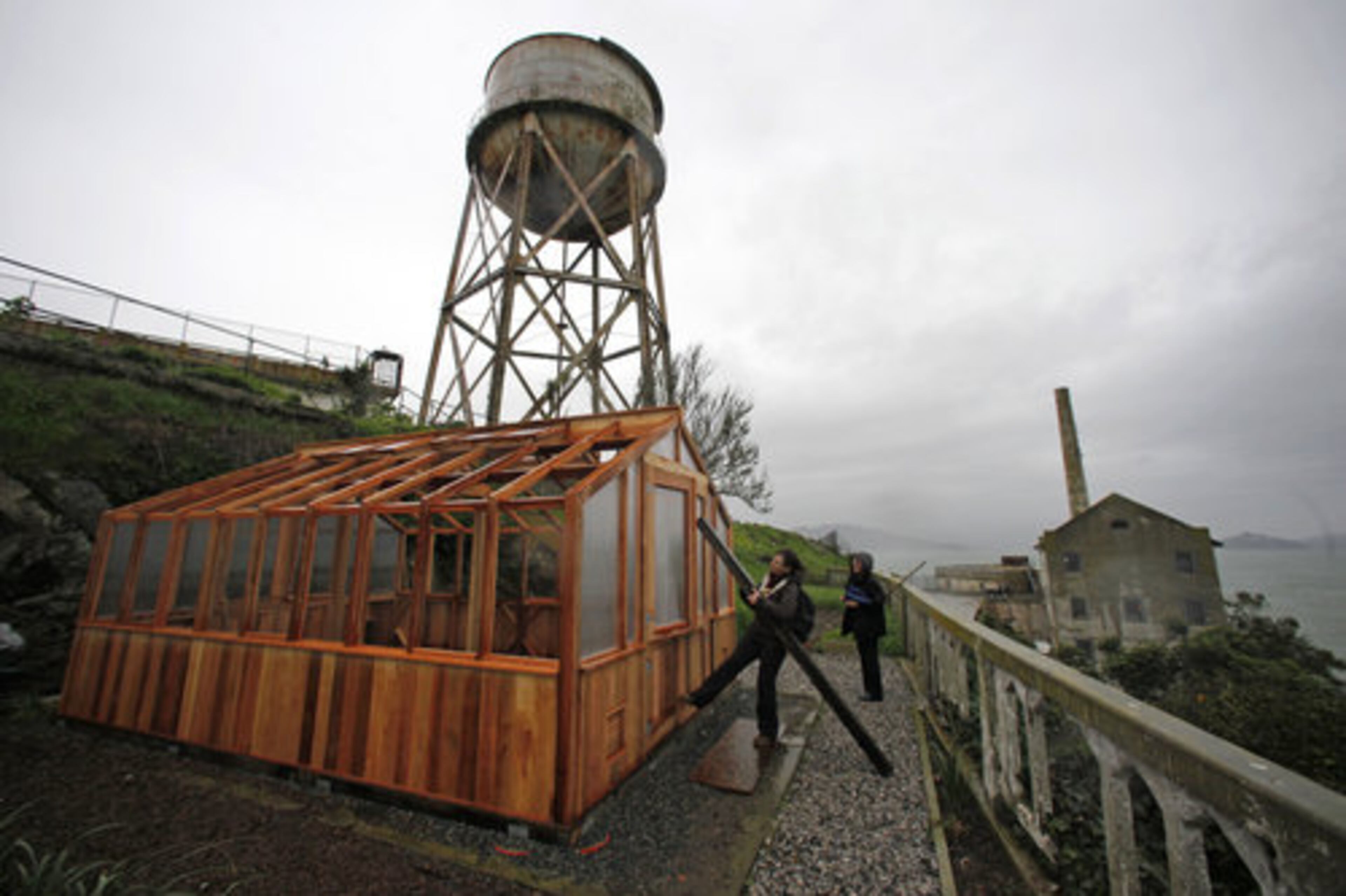 Shelagh Fritz, left, project manager of the Alcatraz Historic Gardens Project, and Dawn Stranne, right, of the Gardens Conservancy look over a new greenhouse under construction near the water tower and power plant, right, on Alcatraz Island in San Francisco.