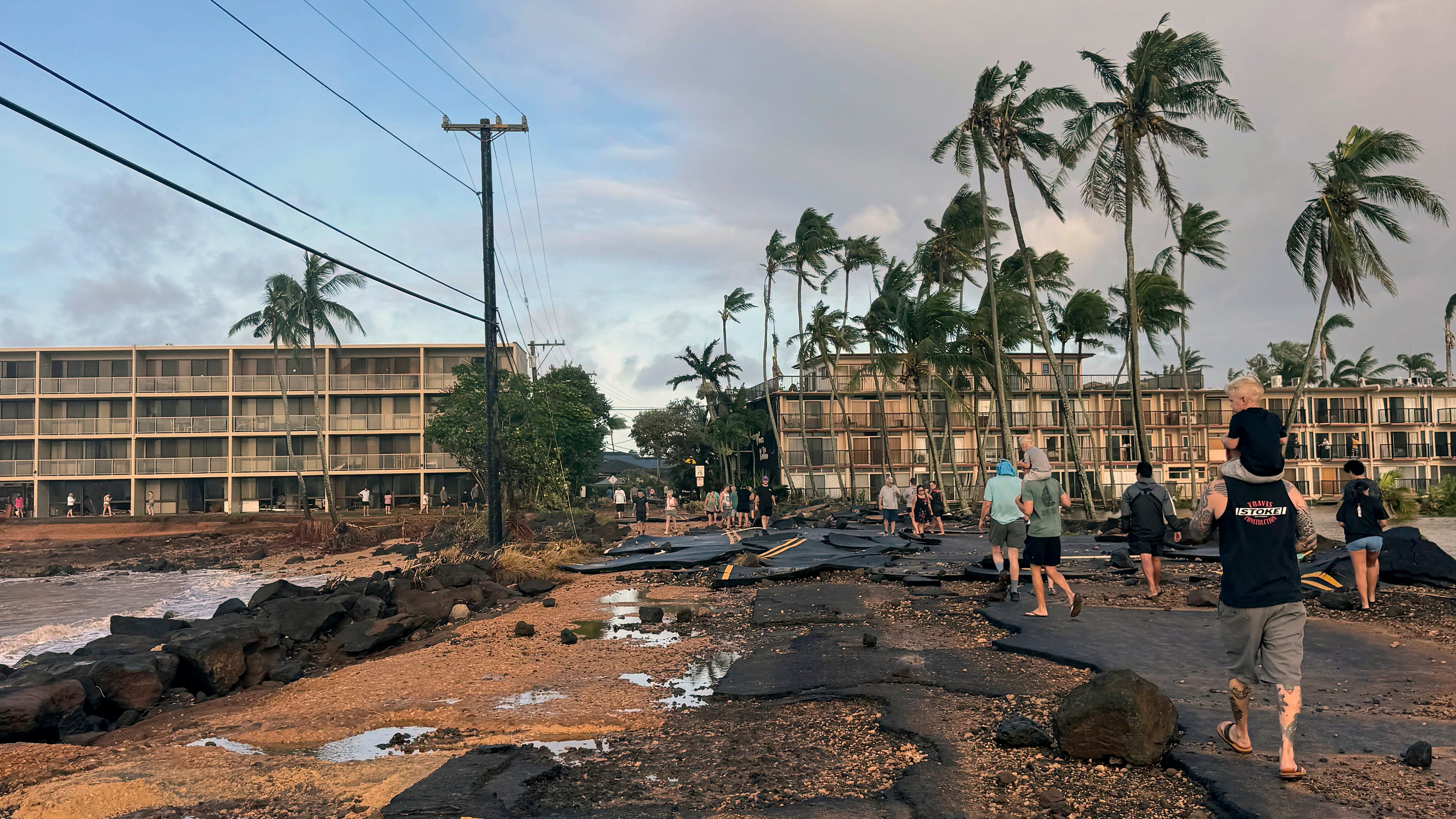 This photo taken with a smartphone, People walk past damage caused by Hurricane Lowell on Tuesday, Sept. 8, 2026 in Poʻipū on Kauaʻi's south shore, in Hawaii. (Guy Miller/Honolulu Civil Beat via AP)
