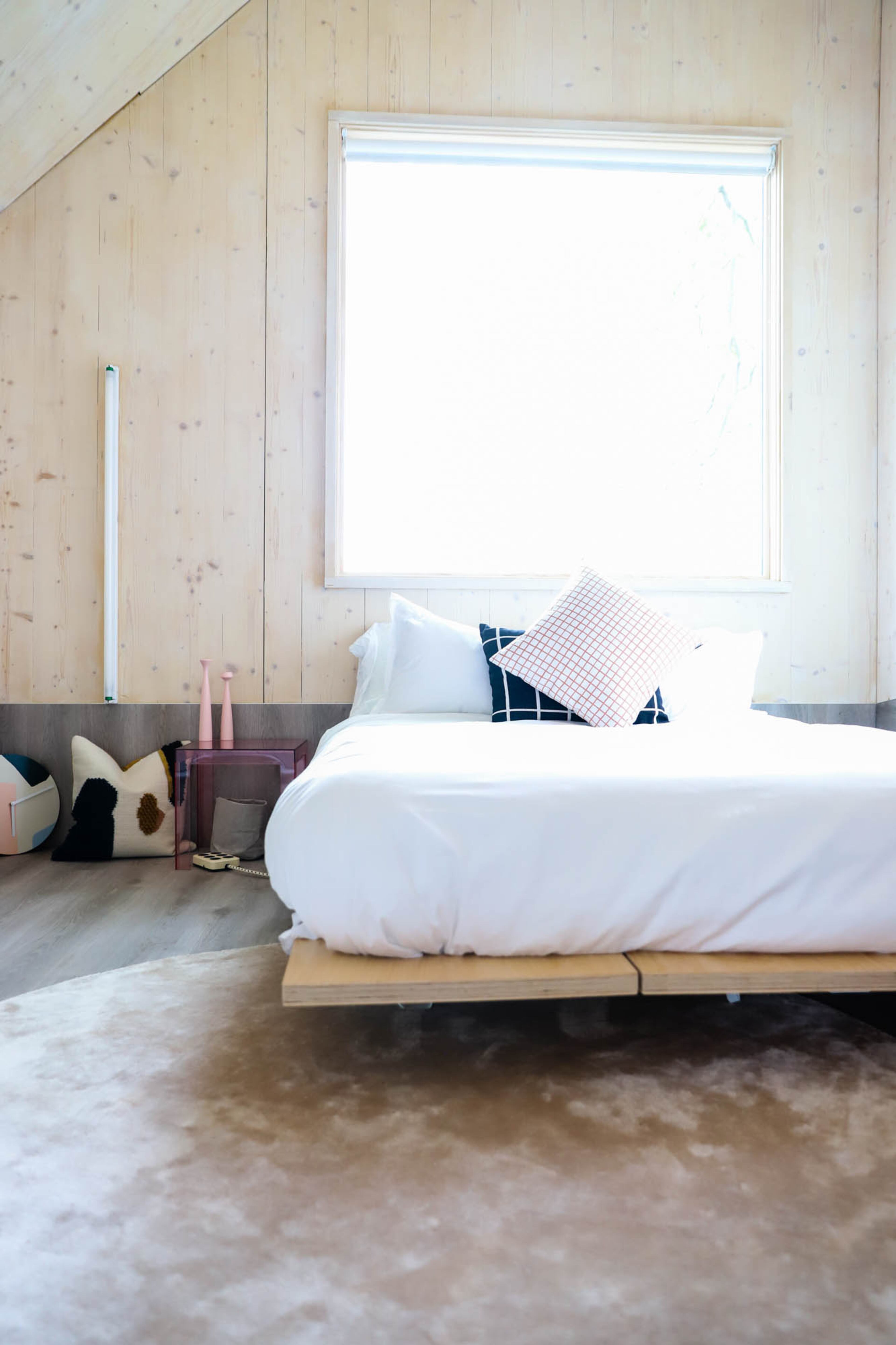 Both bedrooms have a Floyd platform bed, which is made of birch plywood. Kartell's Jolly table in pink is designed by Paolo Rizzatto. Finnish Design Shop's Loop cushion pillows are designed by Ferm Living. The vinyl tile flooring from Johnsonite is in patina ash gray.