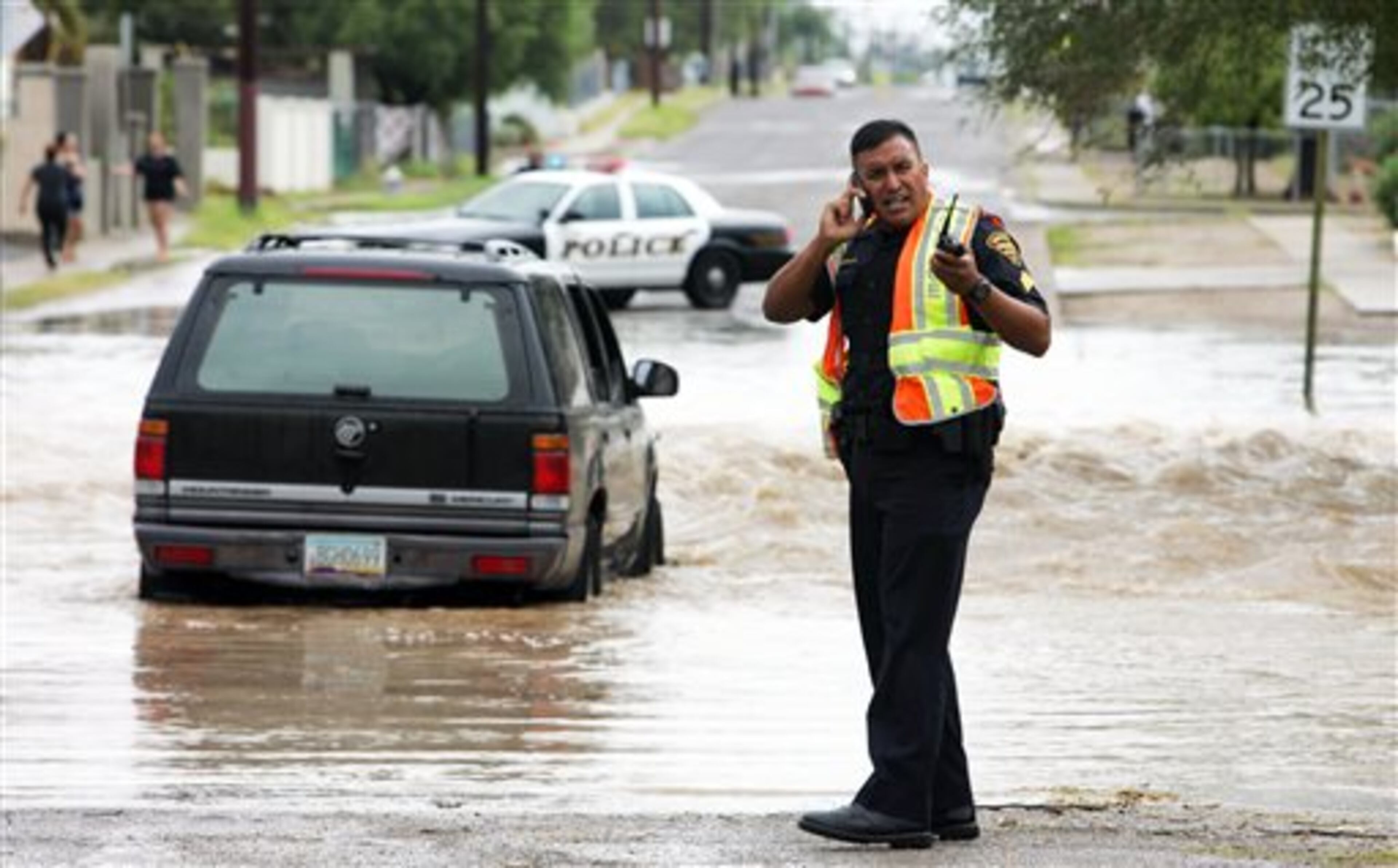 A police officer communicates at the scene where a vehicle is stranded in floodwaters in Tucson, Ariz., on Monday Sept. 8, 2014. The occupants were walked out by Tucson firefighters. Gov. Jan Brewer has declared a statewide emergency in Arizona's most populous county because of flooding from major storms that dropped record rainfall. (AP Photo/Arizona Daily Star, Rick Wiley) LOCAL TV OUT; MANDATORY CREDIT