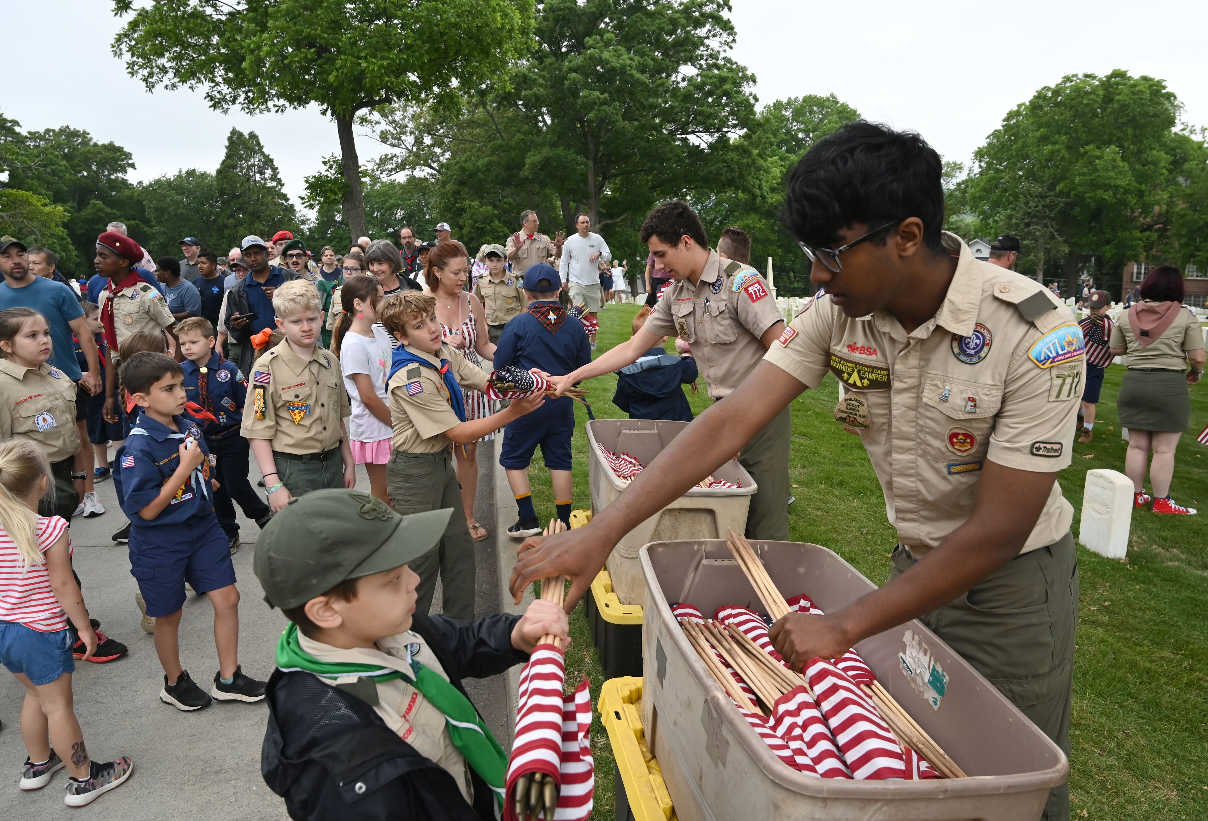 Scouts Landon Hicks and Gowtham Parthasarathi, right, hand out American flags during the Memorial Day Flag Placement event at Marietta National Cemetery on Saturday, May 23, 2026, in Marietta. Scouting groups in the community place more than 18,000 U.S. veteran grave flags at Marietta National Cemetery each year on the Saturday before Memorial Day, helping prepare for Monday’s ceremony. The long-running service project—organized with the National Memorial Day Association of Georgia—also gives youth and adults an opportunity to honor fallen service members and learn about their sacrifices and the area’s history. (Hyosub Shin/AJC)
