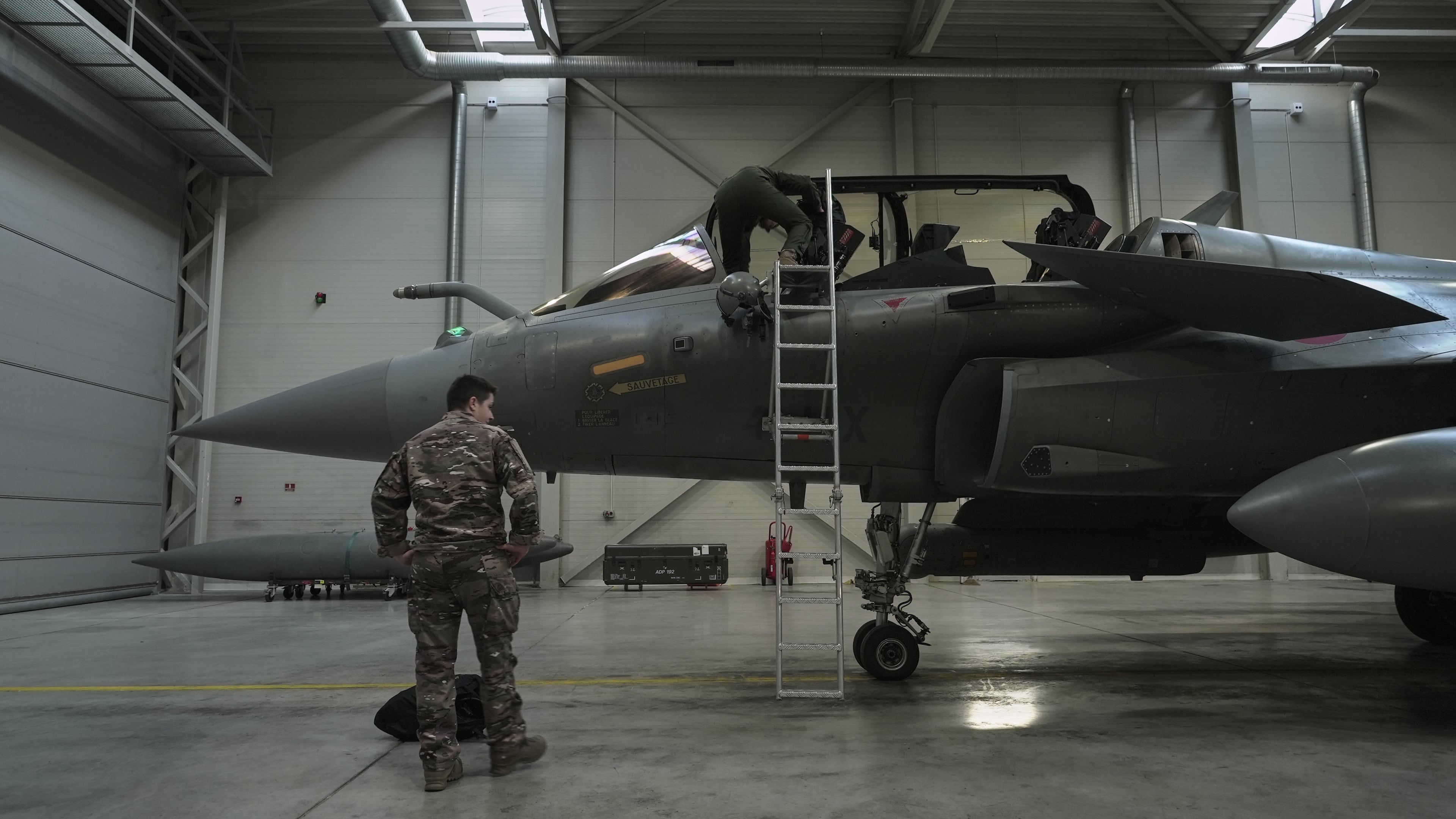 A flight-crew member climbs into the cockpit of a French air force Rafale fighter jet stationed on a NATO air-policing mission at the Siauliai Air Base in Lithuania as another member of the French detachment stands at the foot of the ladder on Sunday, April 19, 2026 (AP Photo/John Leicester)