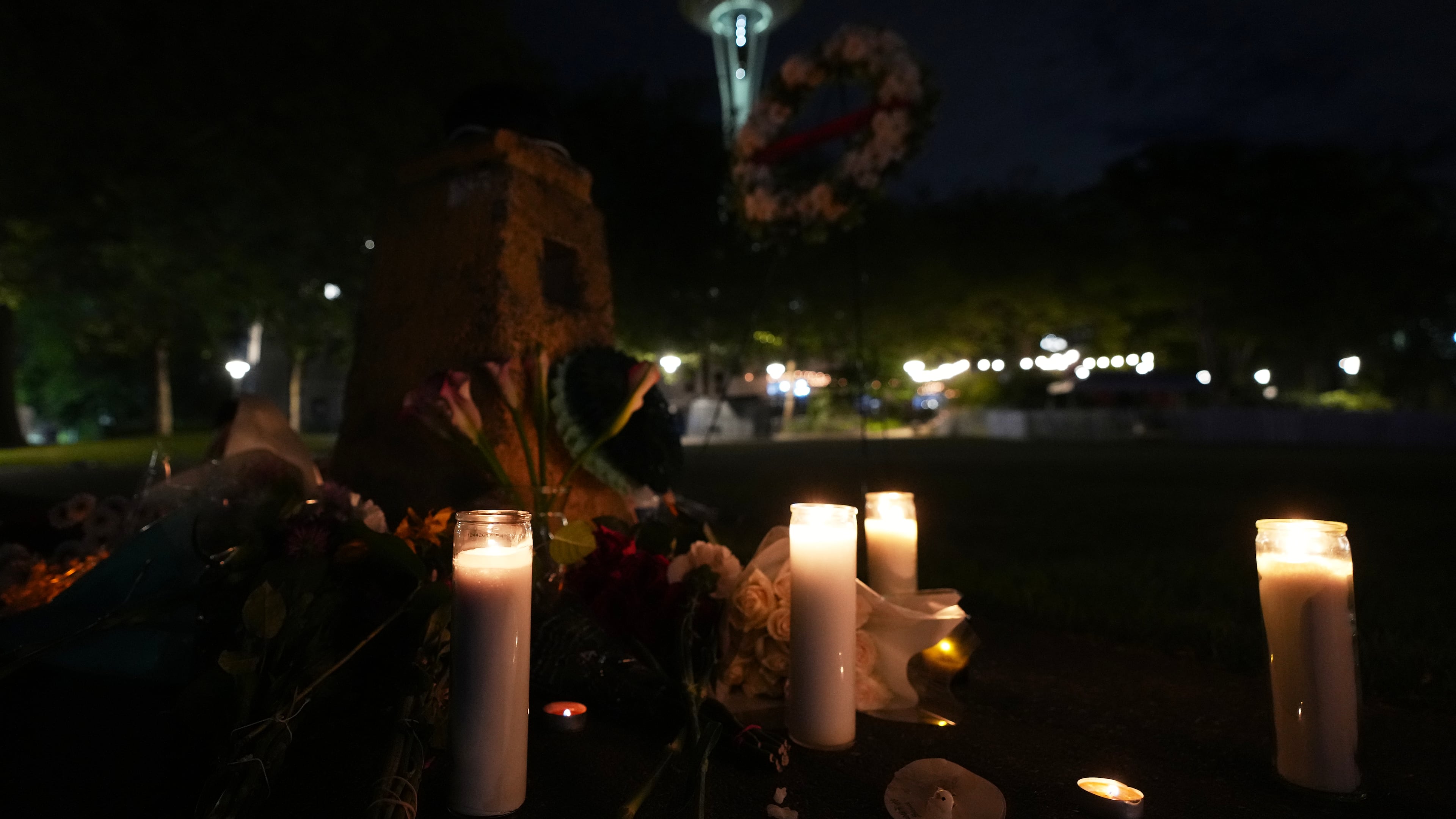 Flowers and candles are seen placed with the Space Needle at background, during the vigil for victims the day after a shooting at Seattle Center during the Bite of Seattle food festival, Monday, July 27, 2026, in Seattle. (AP Photo/Lindsey Wasson)
