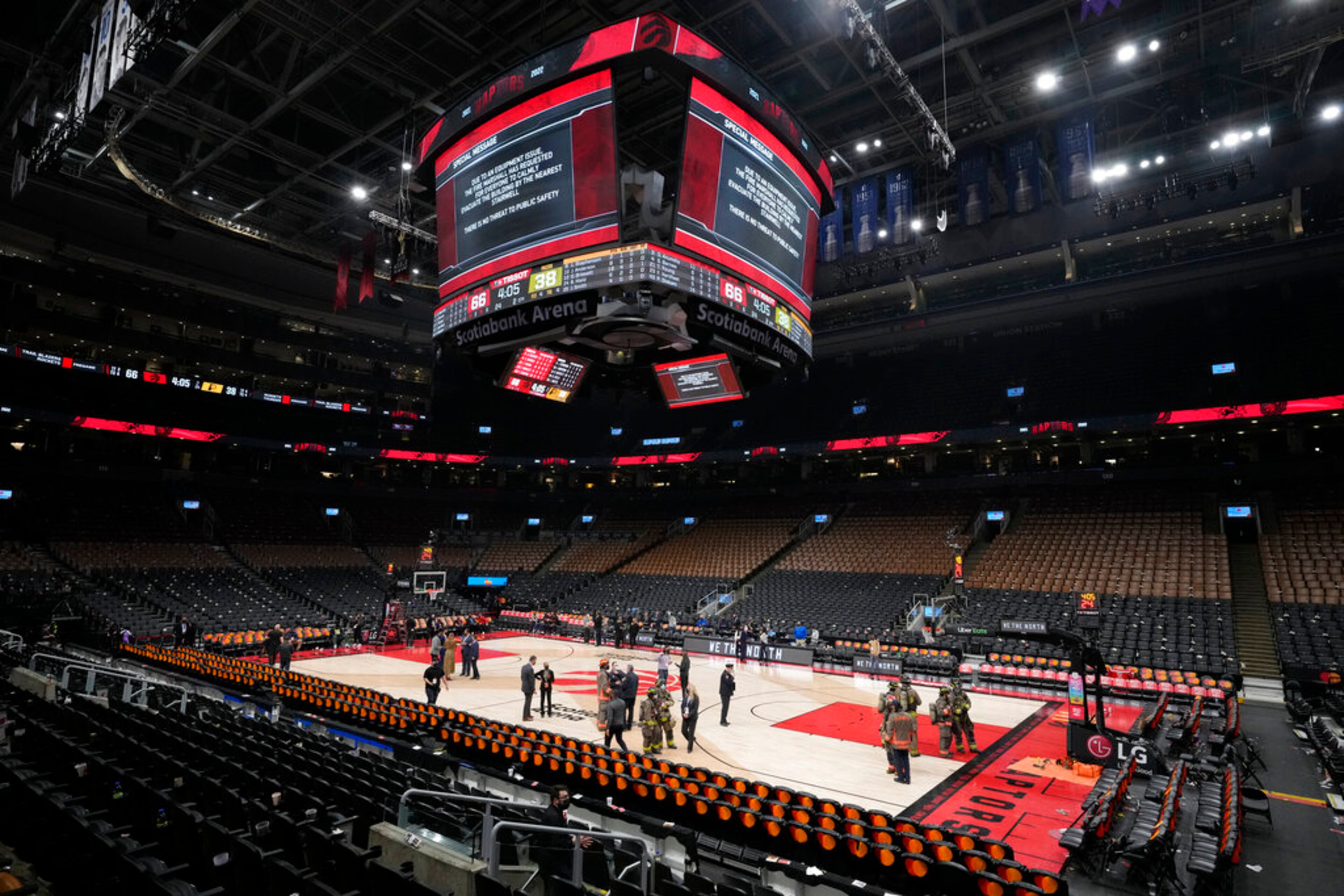 Firefighters and fire department officials stand on the court after play was suspended and the building was evacuated of fans, during the first half of an NBA basketball game between the Toronto Raptors and the Indiana Pacers on Saturday, March 26, 2022, in Toronto. (Frank Gunn/The Canadian Press via AP)