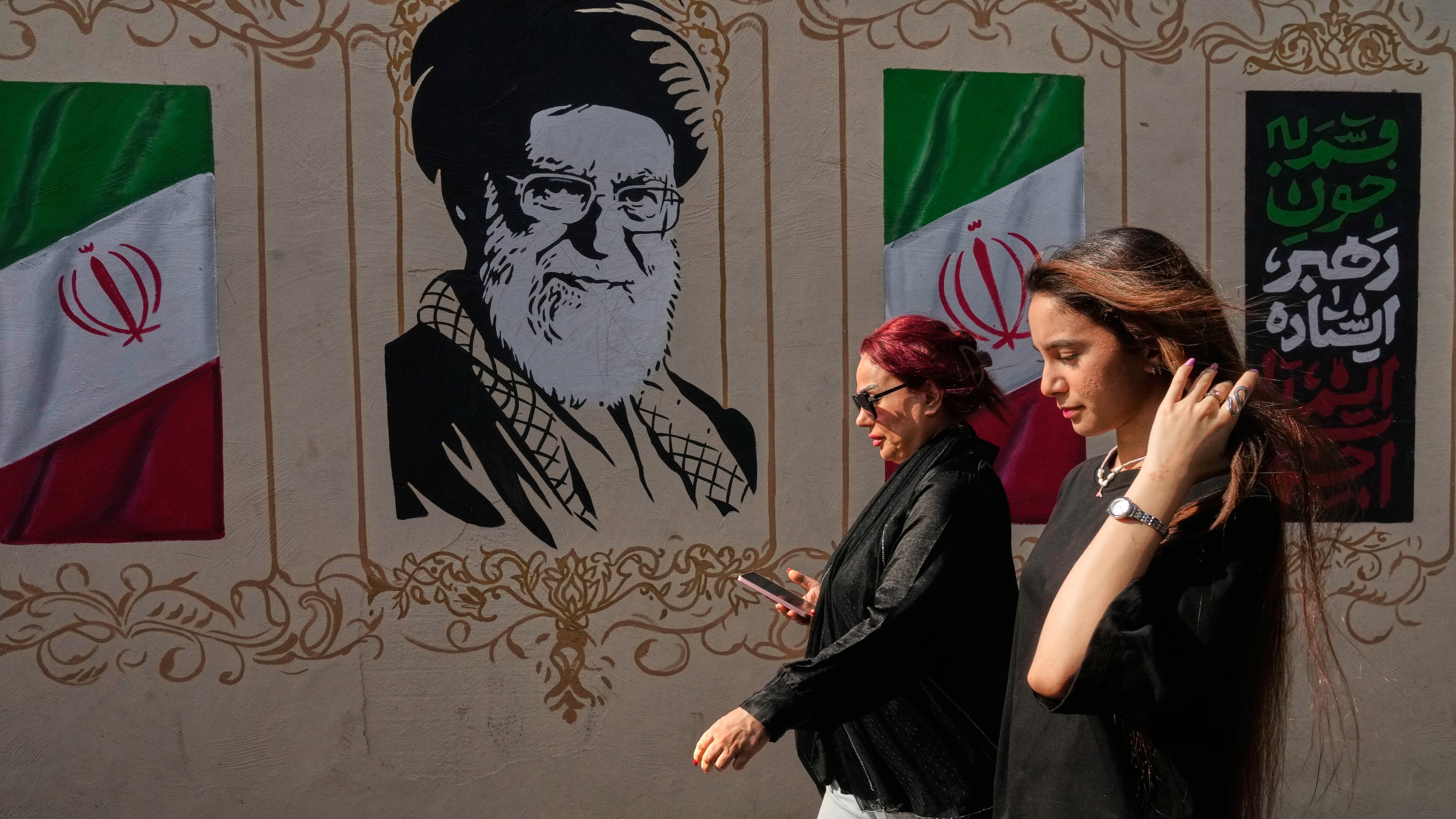 Women walk past a portrait of the late Iranian Supreme Leader Ayatollah Ali Khamenei, who was killed in the U.S. and Israel strike on Feb. 28, and images of the Iranian flag, on a sidewalk in downtown Tehran, Iran, Thursday, Aug. 20, 2026. (AP Photo/Vahid Salemi)