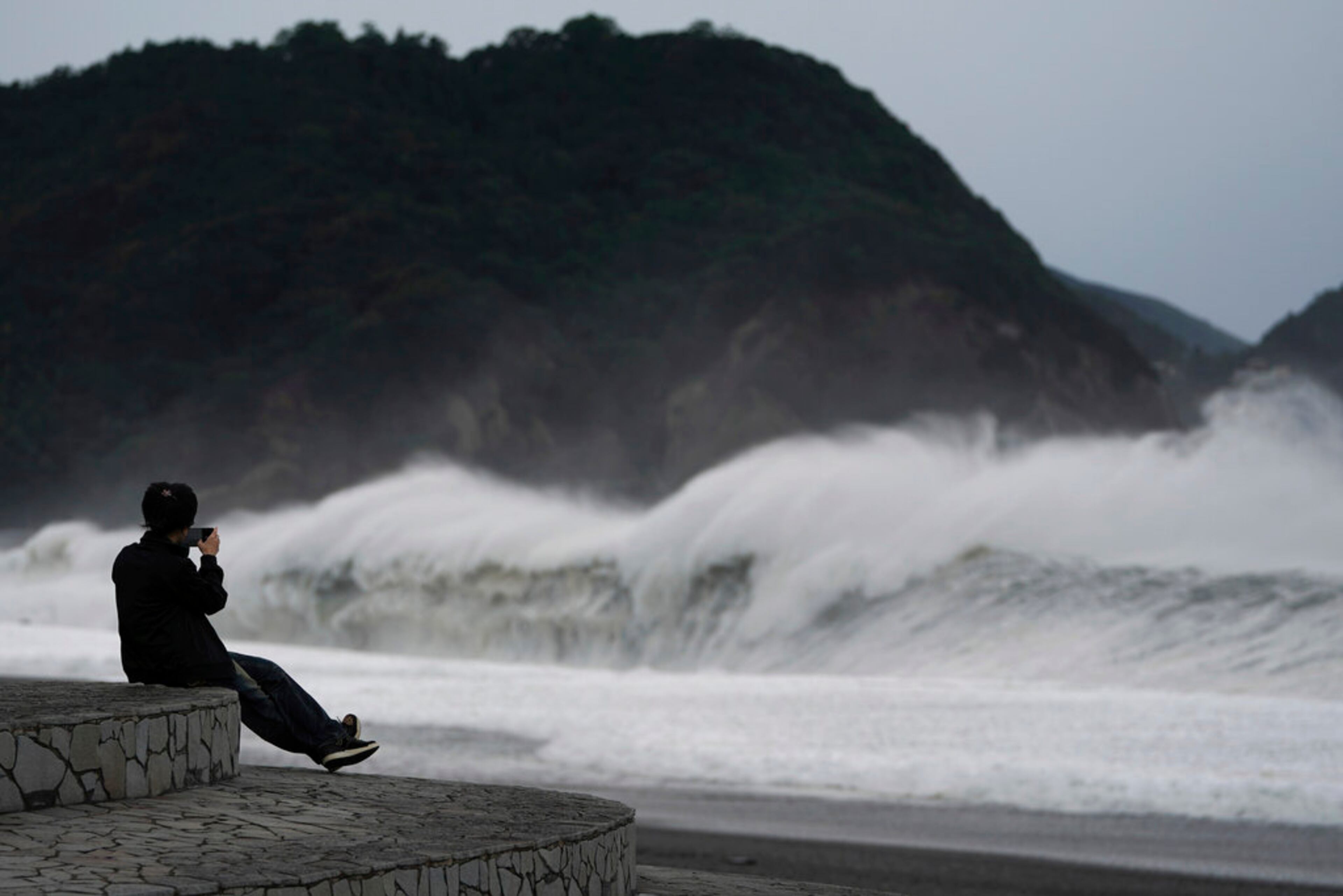 A woman films surging waves as Typhoon Hagibis approaches at a beach in Kumano, Mie prefecture, central Japan Saturday, Oct. 12, 2019. (AP Photo/Toru Hanai)