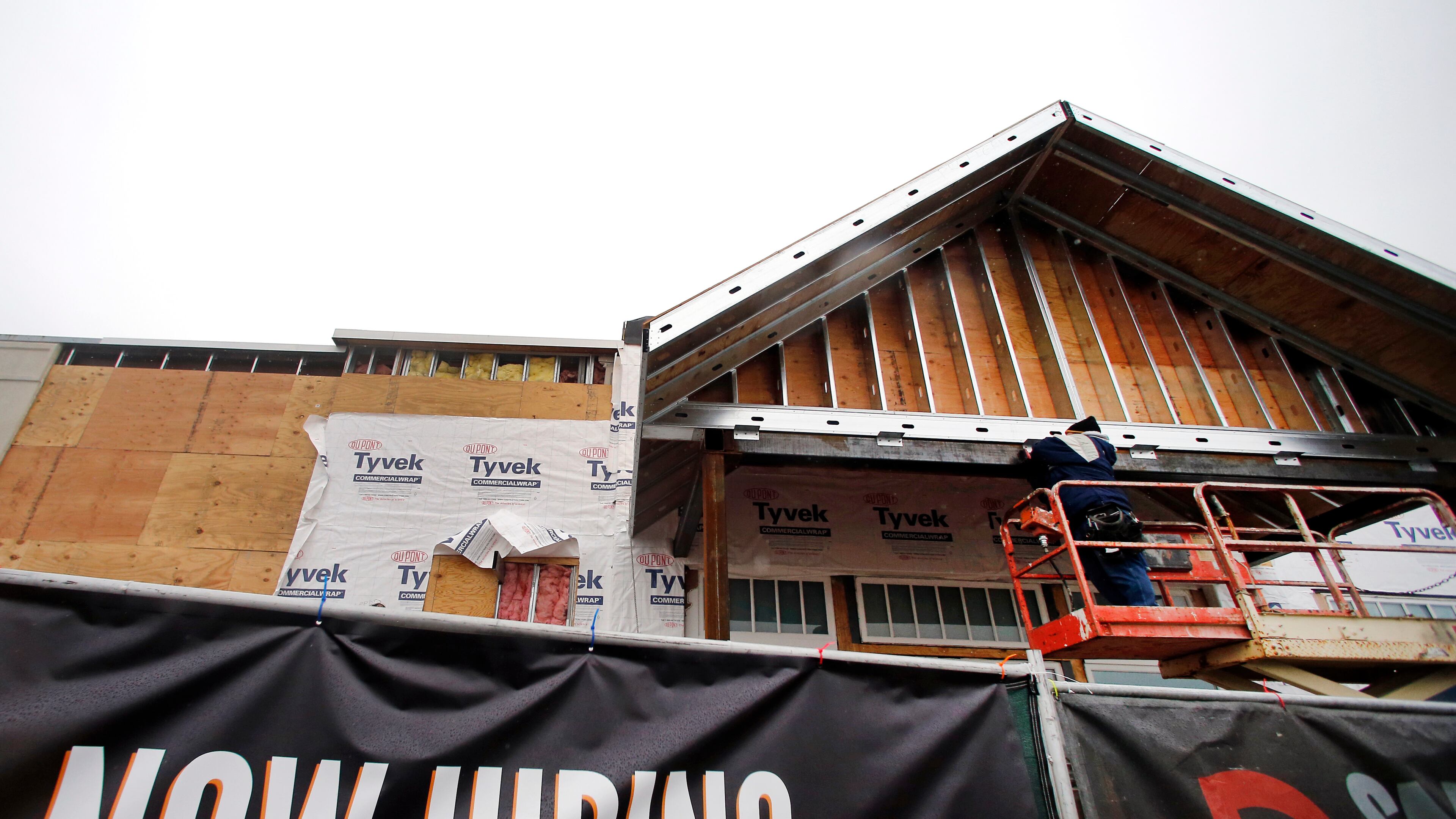 FILE - In this Jan. 12, 2015 file photo, a now hiring sign hangs nearby as a builder works on a commercial property under construction in Peabody, Mass. The National Association for Business Economics has boosted its outlook for U.S. economic improvement in 2015 and 2016, particularly for job growth, according to a report released Monday, March 30, 2015. (AP Photo/Elise Amendola, File)
