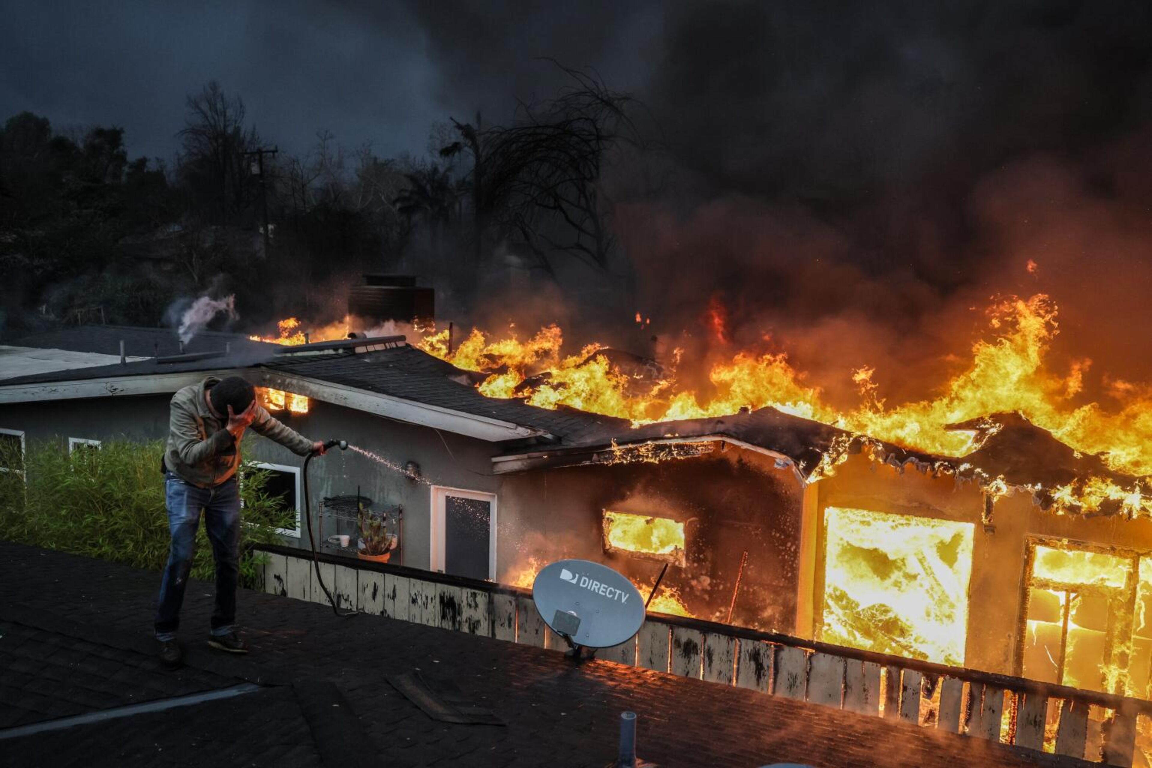 Steve Salinas shields from intense heat as he hoses down a neighbors rooftop on Sinaloa Ave. as the Eaton Fire continues to grow on Wednesday, Jan. 8, 2025, in Altadena, California. (Robert Gauthier/Los Angeles Times/TNS)