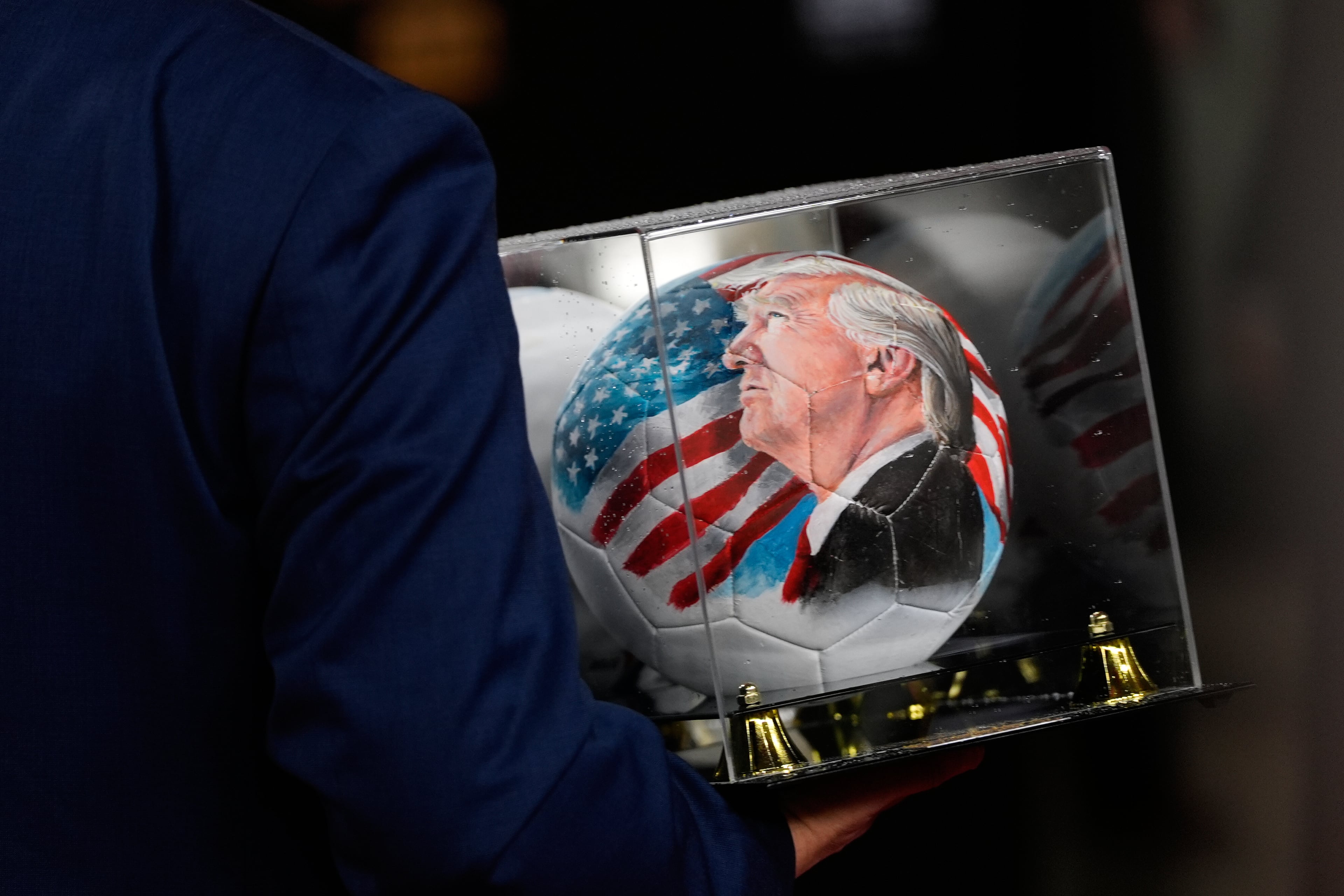 A person carries a soccer ball with a picture of President Donald Trump before the draw for the 2026 soccer World Cup at the Kennedy Center in Washington, Friday, Dec. 5, 2025. (AP Photo/Julia Demaree Nikhinson)