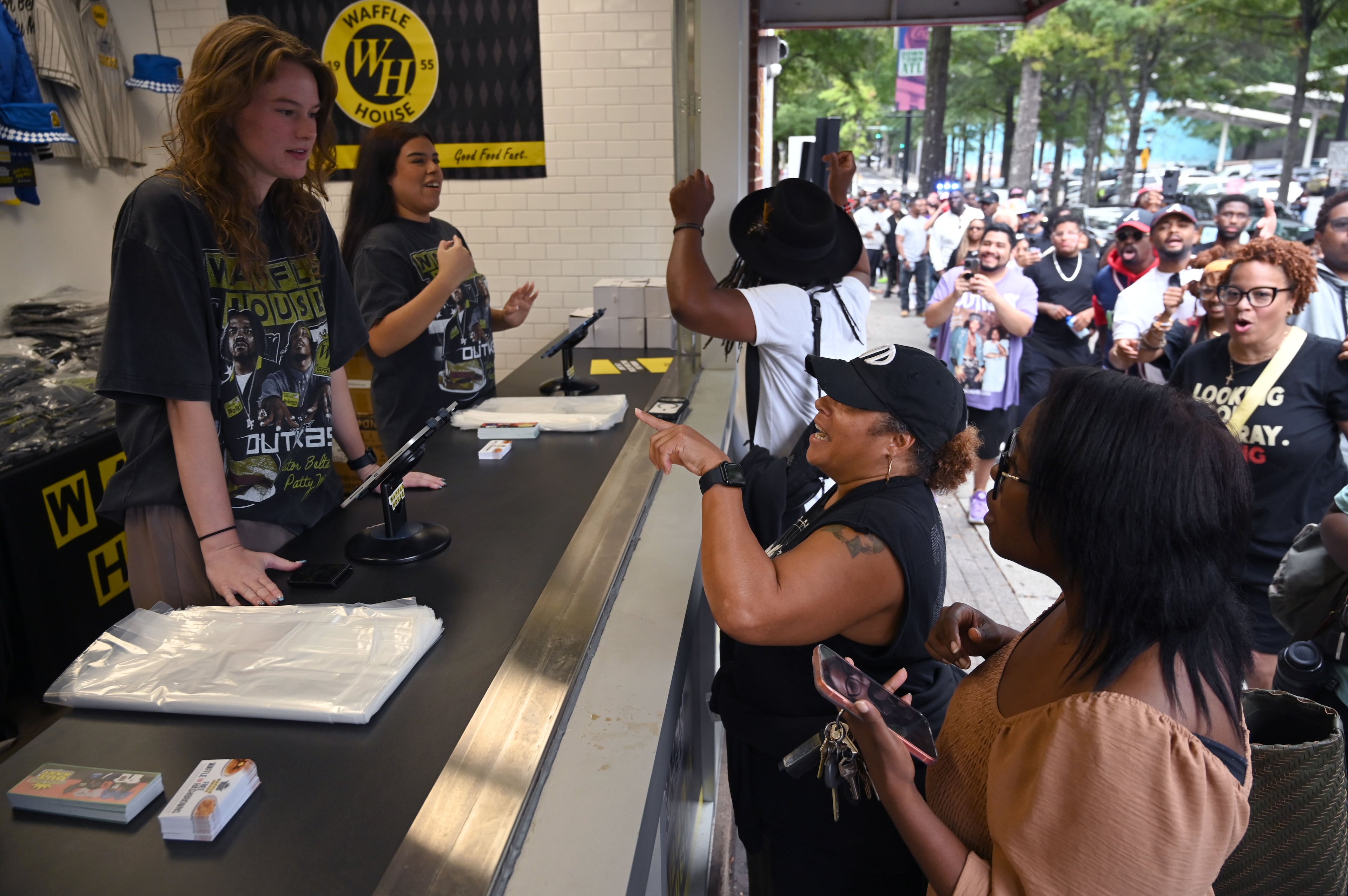 Customers and Outkast fans Melanie Williams (foreground), Heather King (center) and Dedren Snead get their limited-edition merchandise from the Outkast and Waffle House collaboration during the exclusive launch event. (Hyosub Shin/AJC)