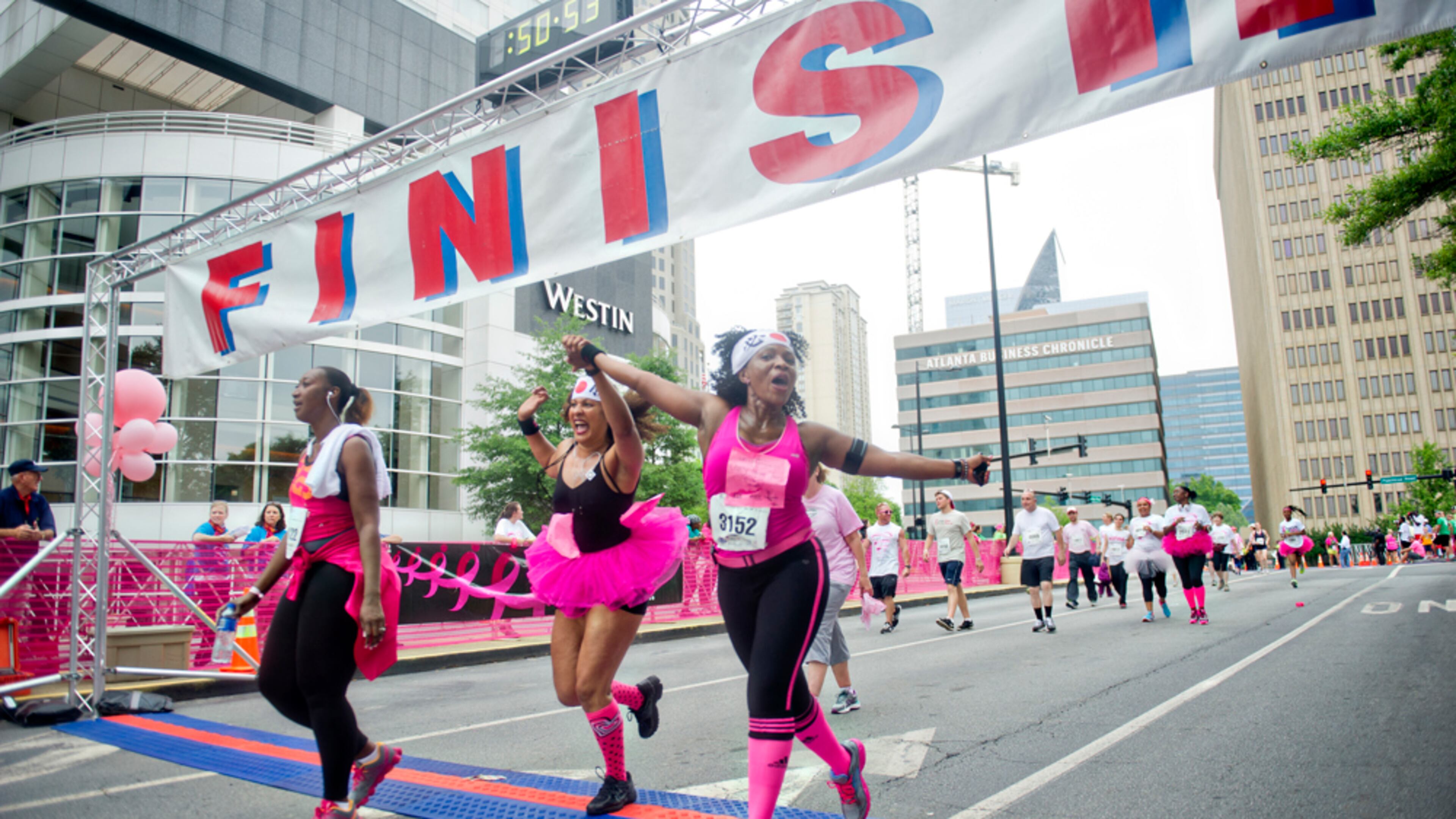 Chi Michaels (right) and Leesa Mendes hold hands as they cross the finish line for the Susan G. Komen Race for the Cure at Lenox Square Mall on Saturday, May 10, 2014.