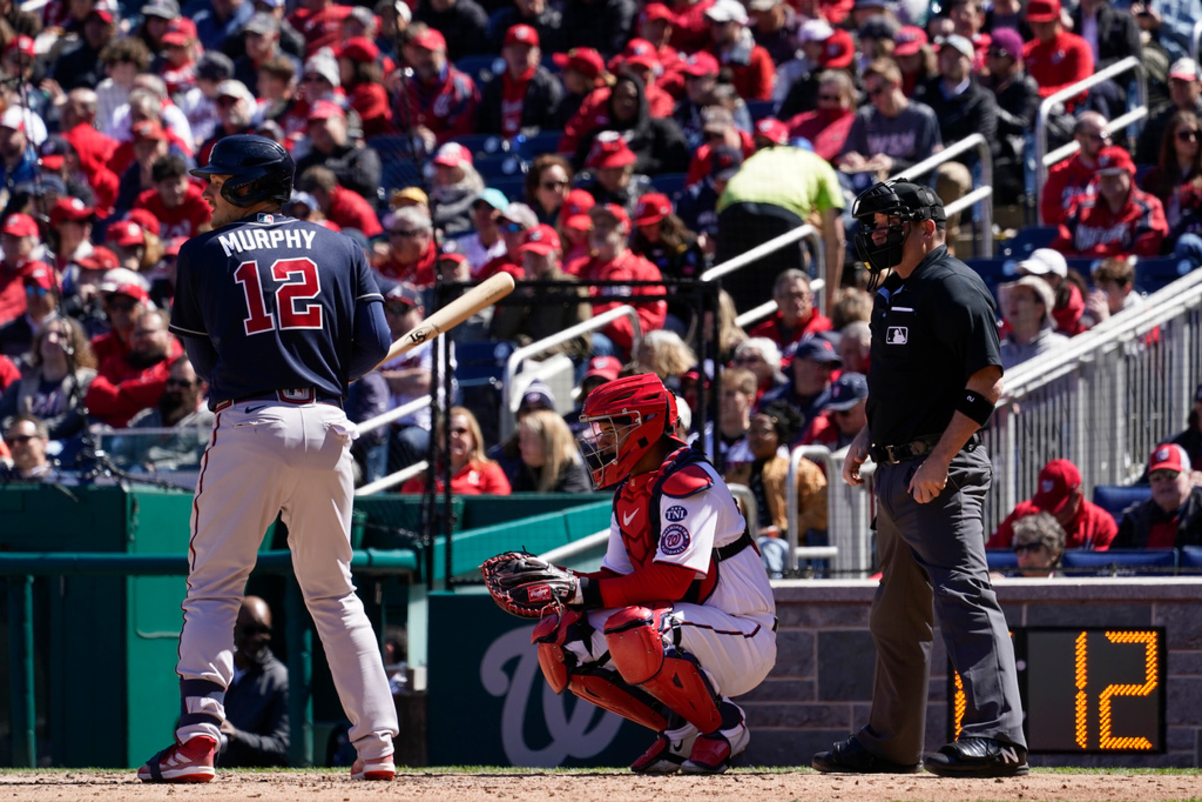 A pitch clock, bottom right, is seen behind Atlanta Braves' Sean Murphy, from left, Washington Nationals catcher Keibert Ruiz and home plate umpire Dan Bellino during an opening day baseball game at Nationals Park, Thursday, March 30, 2023, in Washington. (AP Photo/Alex Brandon)