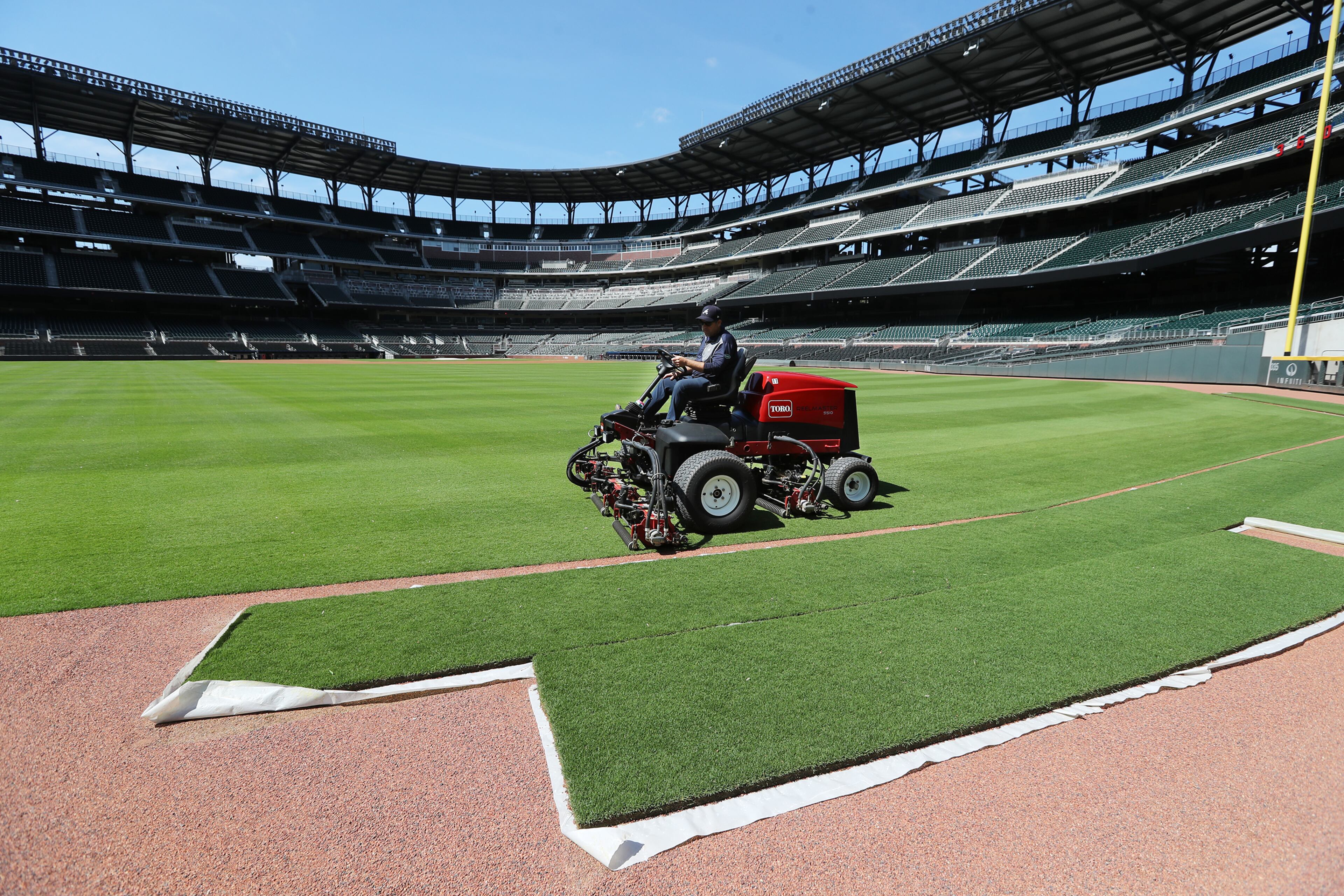 Field manager Anthony DeFeo, mowing left field at Truist Park on Wednesday, passes by extra sod used for any needed repairs.