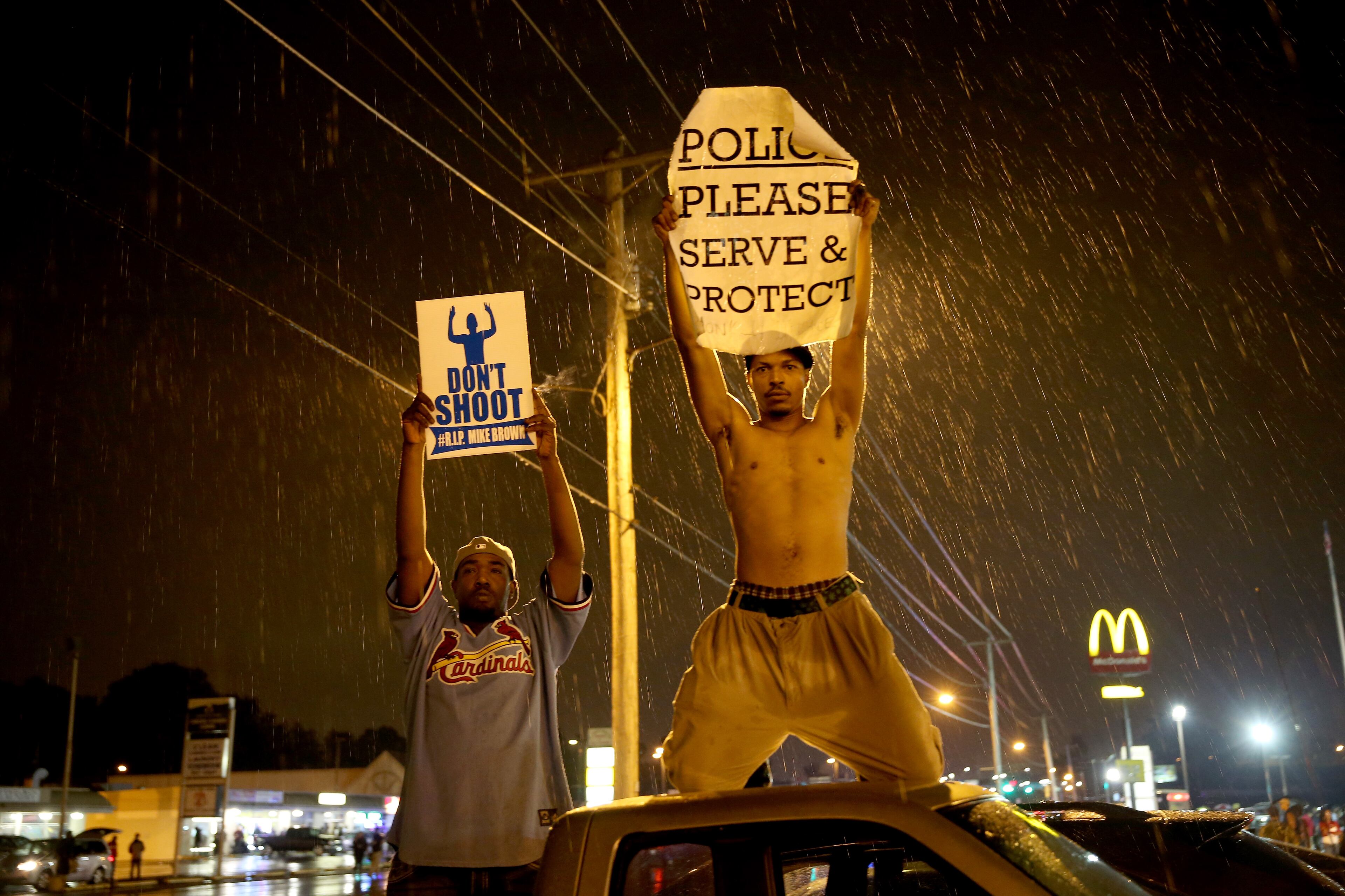 FERGUSON, MO - AUGUST 16: Demonstrators protesting the shooting death of Michael Brown hold signs on August 16, 2014 in Ferguson, Missouri. Violent outbreaks have taken place in Ferguson since the shooting death of Michael Brown by a Ferguson police officer on August 9th. (Photo by Joe Raedle/Getty Images)