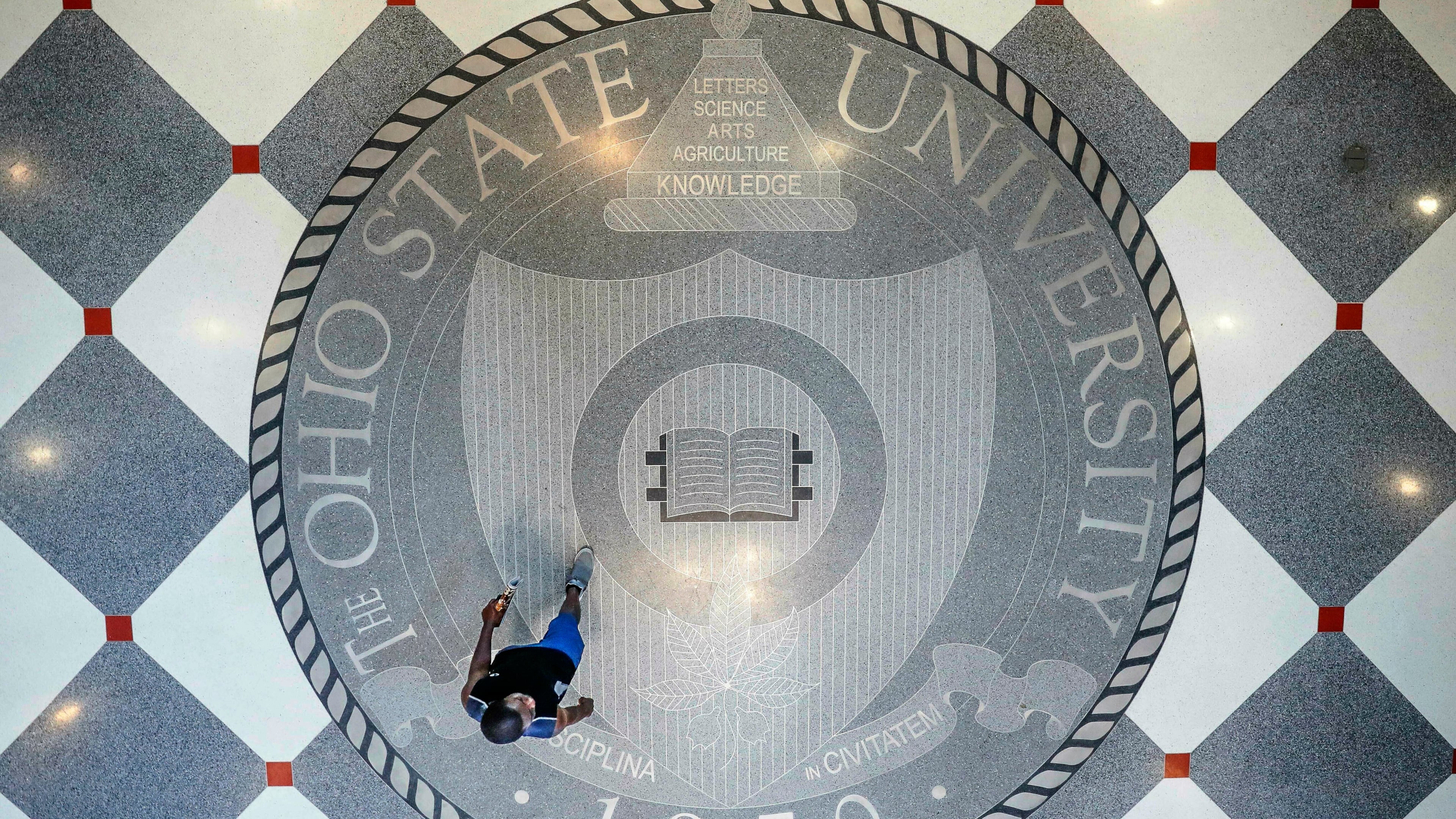 FILE - A person walks over the Ohio State University's emblem in the campus student union, May 18, 2019, in Columbus, Ohio. (AP Photo/John Minchillo, File)