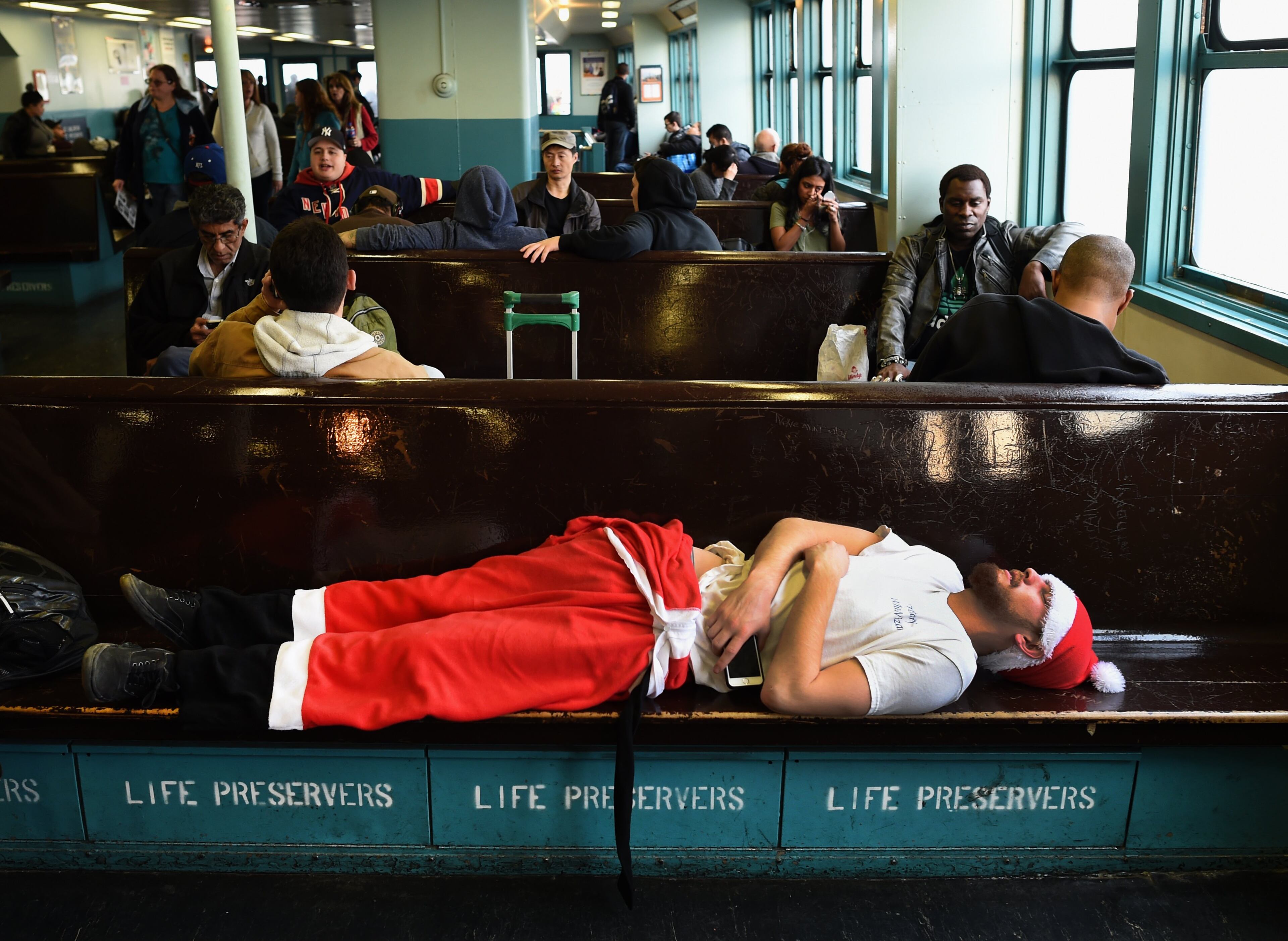 A man dressed in a Santa outfit sleeps on the Staten Island during the SantaCon in New York City on December 12, 2015. SantaCon is an event where groups of men and woman dress as Santa. AFP PHOTO / TIMOTHY A. CLARY / AFP / TIMOTHY A. CLARY (Photo credit should read TIMOTHY A. CLARY/AFP/Getty Images)