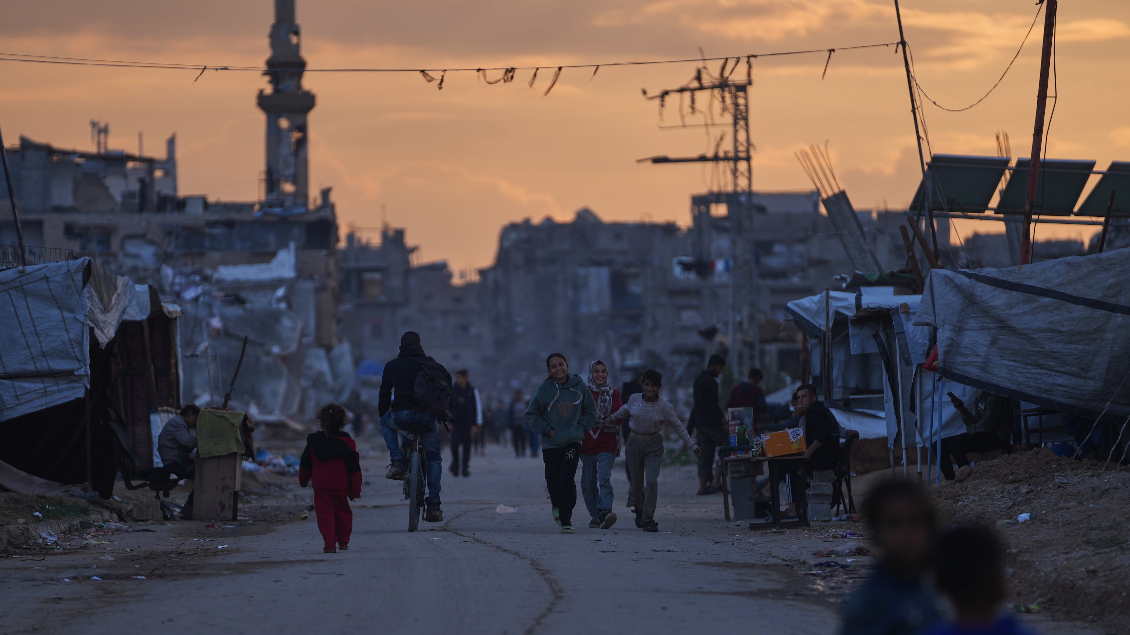 Palestinian youth walk along a tent camp for displaced people as the sun sets in Nuseirat, central Gaza Strip, Friday, Dec. 26, 2025. (AP Photo/Abdel Kareem Hana)