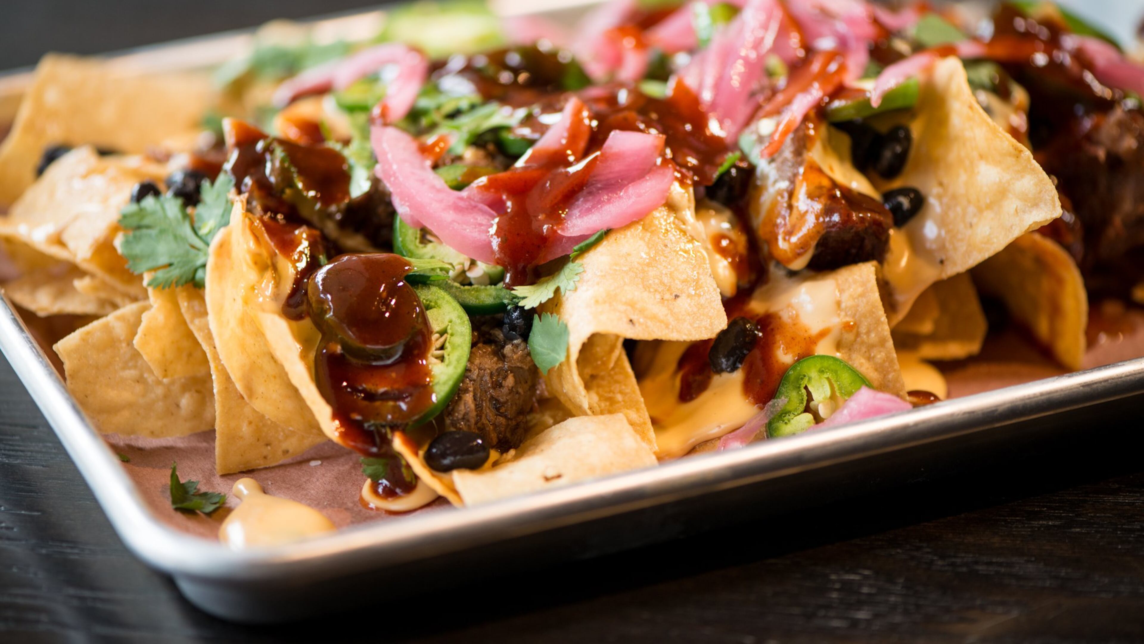 BBQ Nachos, chips and cheese covered with brisket, jalapenos, pickled onions, black beans, cilantro, and BBQ sauce. Photo credit- Mia Yakel.