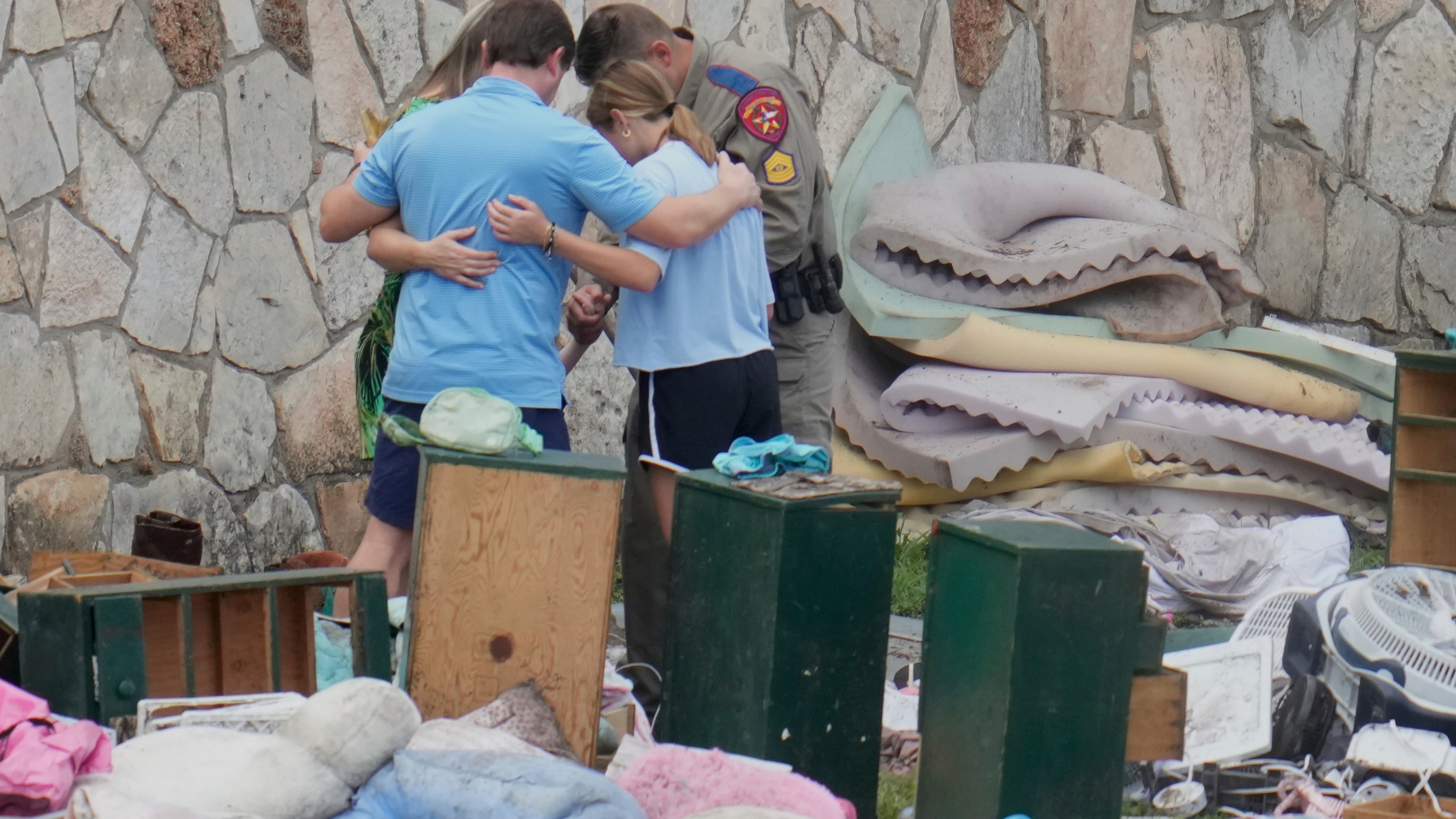 FILE - An officer prays with a family as they pick up items at Camp Mystic in Hunt, Texas on July 9, 2025. (AP Photo/Ashley Landis, file)