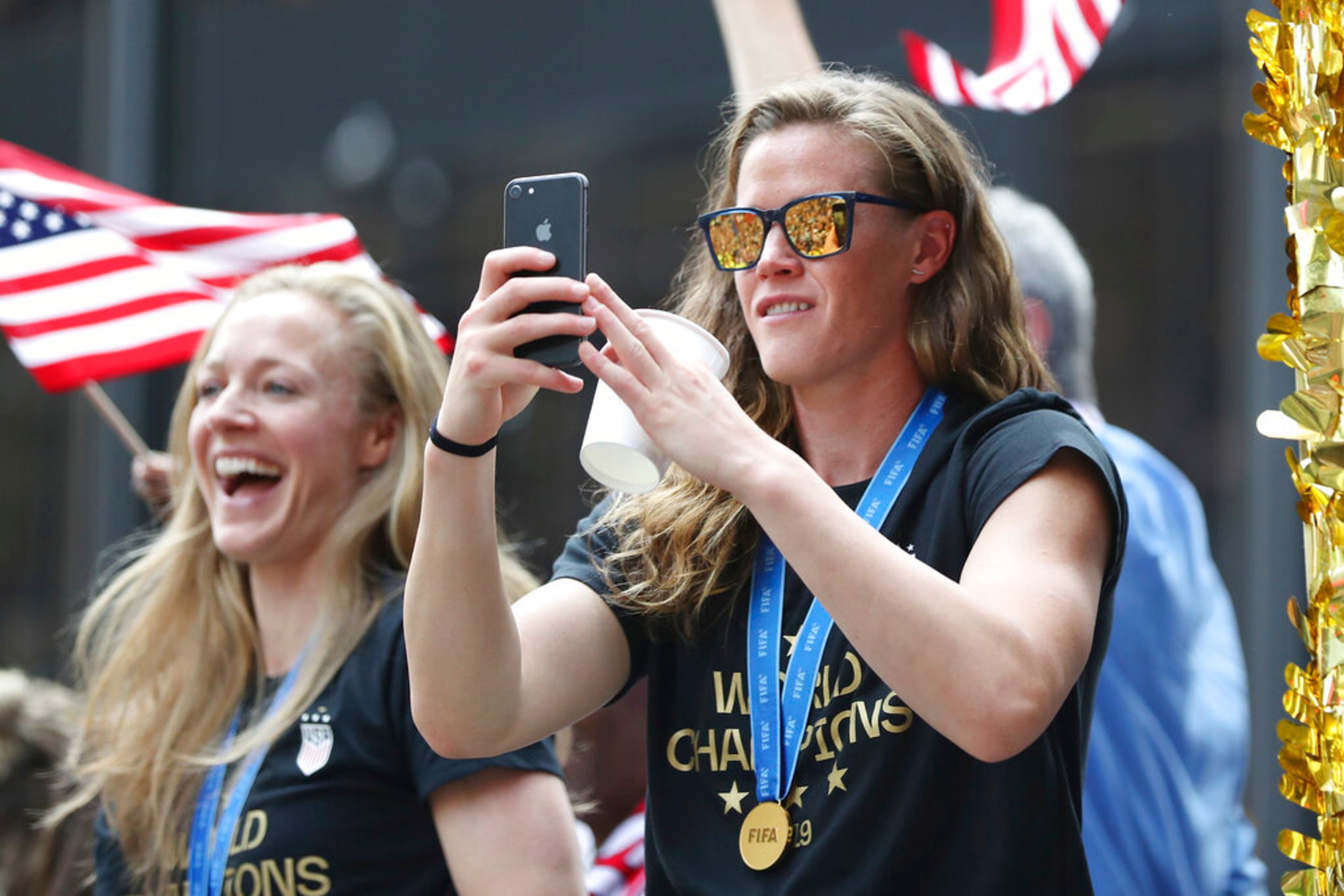 United States goalkeeper Alyssa Naeher, right, takes a photo of the crowd while United States defender Becky Sauerbrunn looks out on a float while being honored with a ticker tape parade along the Canyon of Heroes, Wednesday, July 10, 2019, in New York. The U.S. national team beat the Netherlands 2-0 to capture a record fourth Women's World Cup title. (AP Photo/Steve Luciano)