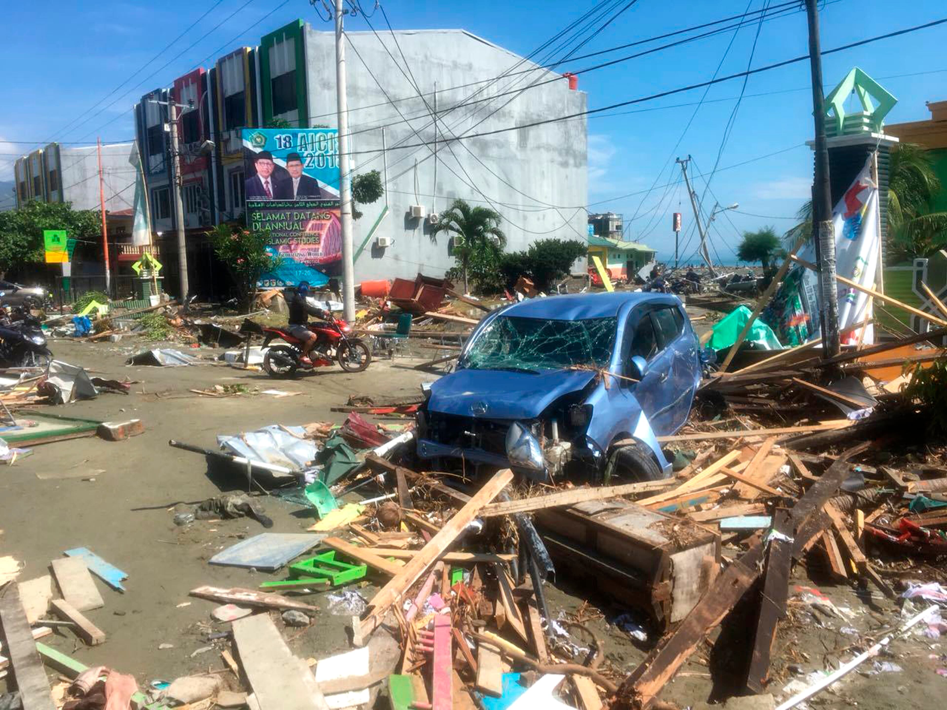 A motorbike passes the wreckage of a car following earthquakes and a tsunami in Palu, Central Sulawesi, Indonesia, Sunday, Sept. 30, 2018. A tsunami swept away buildings and killed large number of people on the Indonesian island of Sulawesi, dumping victims caught in its relentless path across a devastated landscape that rescuers were struggling to reach Saturday, hindered by damaged roads and broken communications. (AP Photo/Tatan Syuflana)