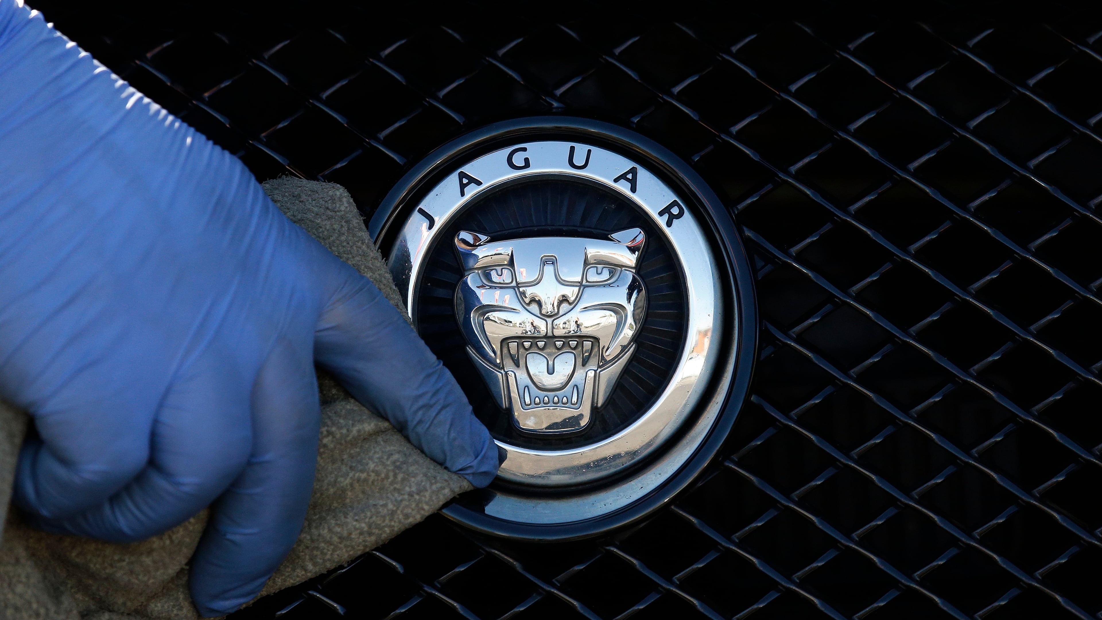 FILE - A worker polishes a Jaguar logo on a car at a Jaguar dealer in London, Wednesday Sept. 28, 2016. (AP Photo/Frank Austin, File)