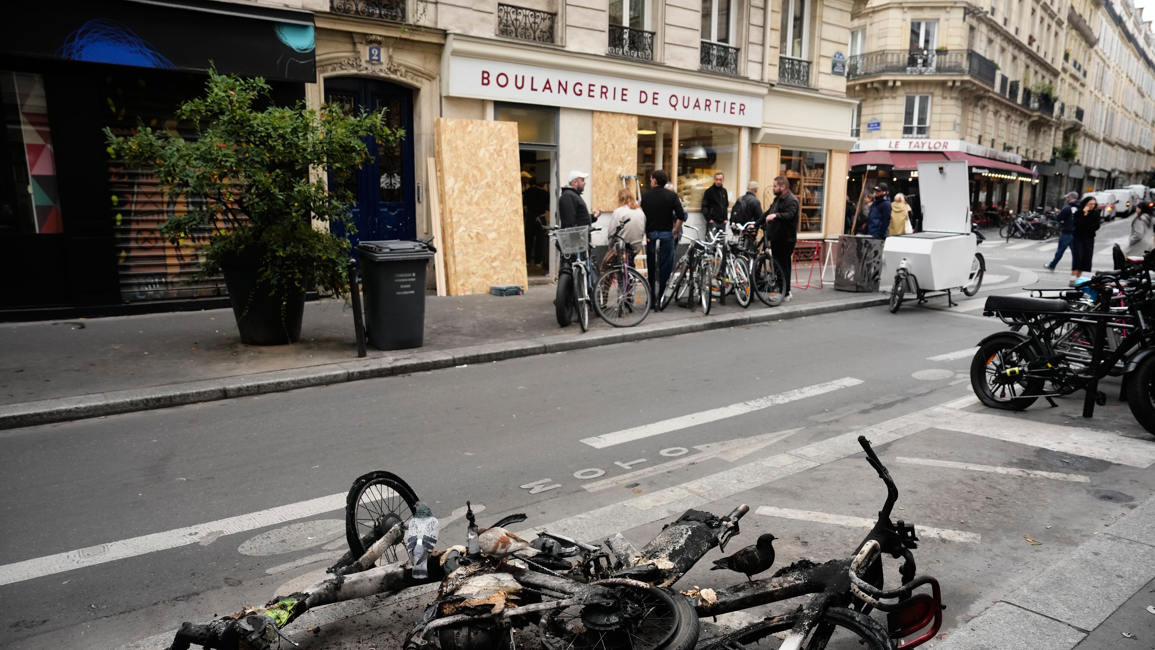 Burned electric bicycles lie on the road near a bakery after weekend protests over the cost of living turned into rioting and looting across France, in Paris, Wednesday, Oct. 21, 2026. (AP Photo/Teresa Suarez)