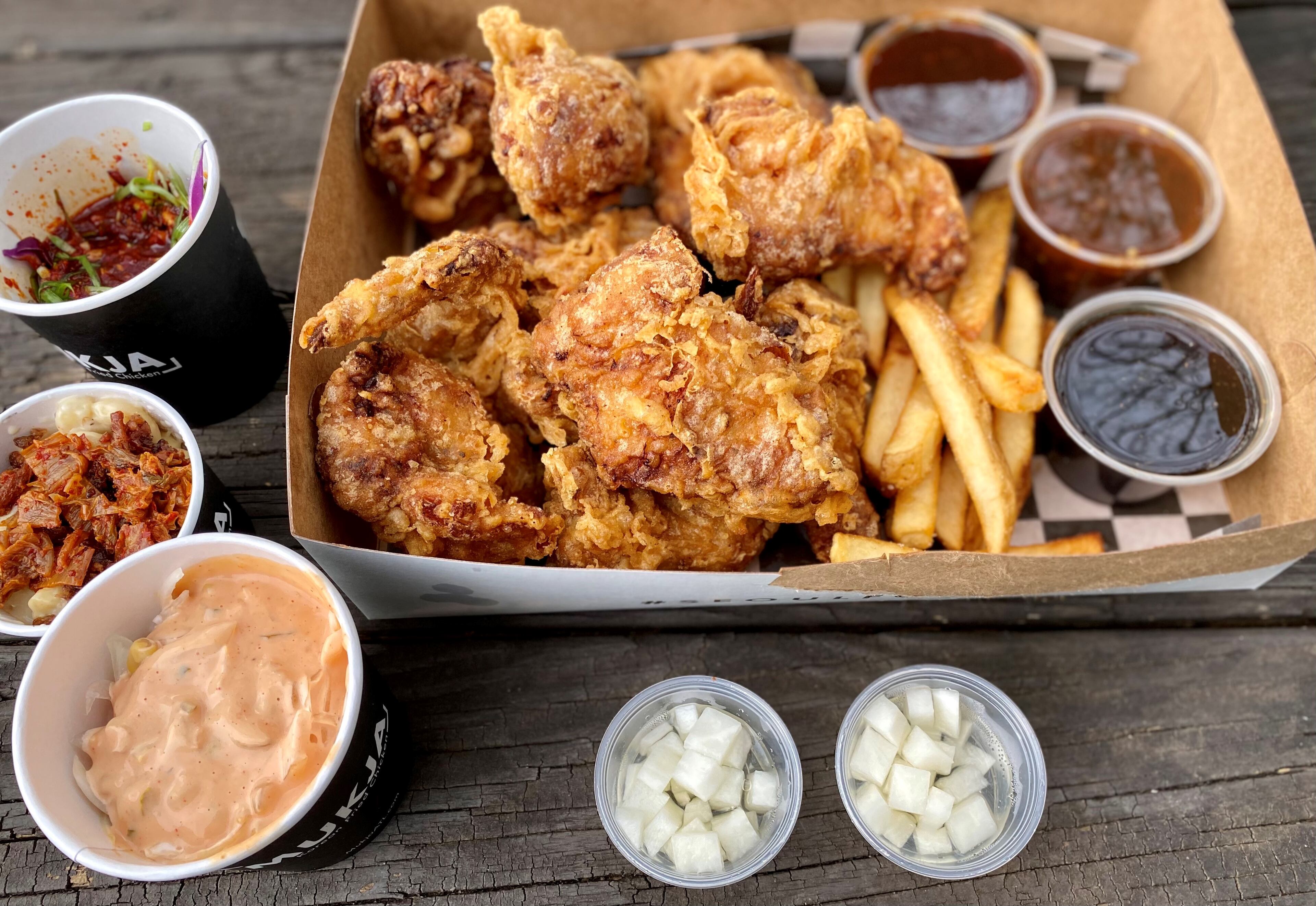 Takeout from Mukja Korean Fried Chicken in Midtown: A whole fried chicken with sauces and fries; pickled radish; and sides, left from the top: Korean slaw, macaroni and cheese with kimchi and bacon, and the Standard, a slaw with onion, corn and Thousand Island spiked with gochujang.
Wendell Brock for The Atlanta Journal-Constitution