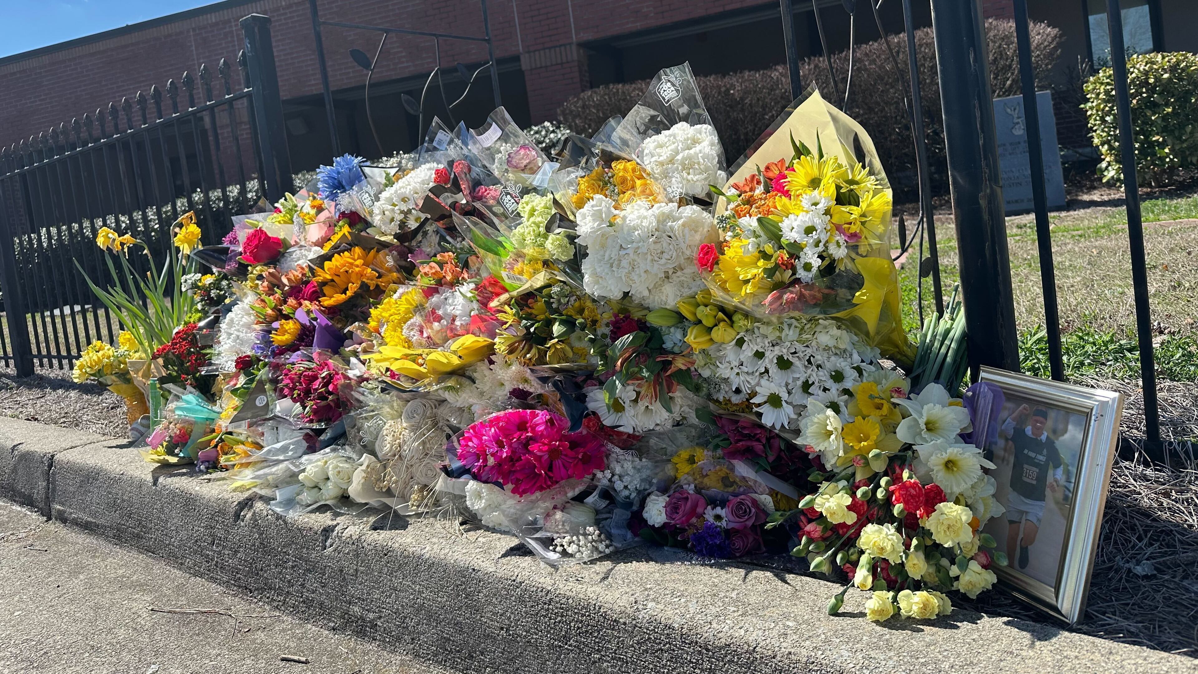 Flowers lie along a fence outside North Hall High School in Gainesville, Ga., on Monday, March 9, 2026. (AP Photo/Emilie Megnien)