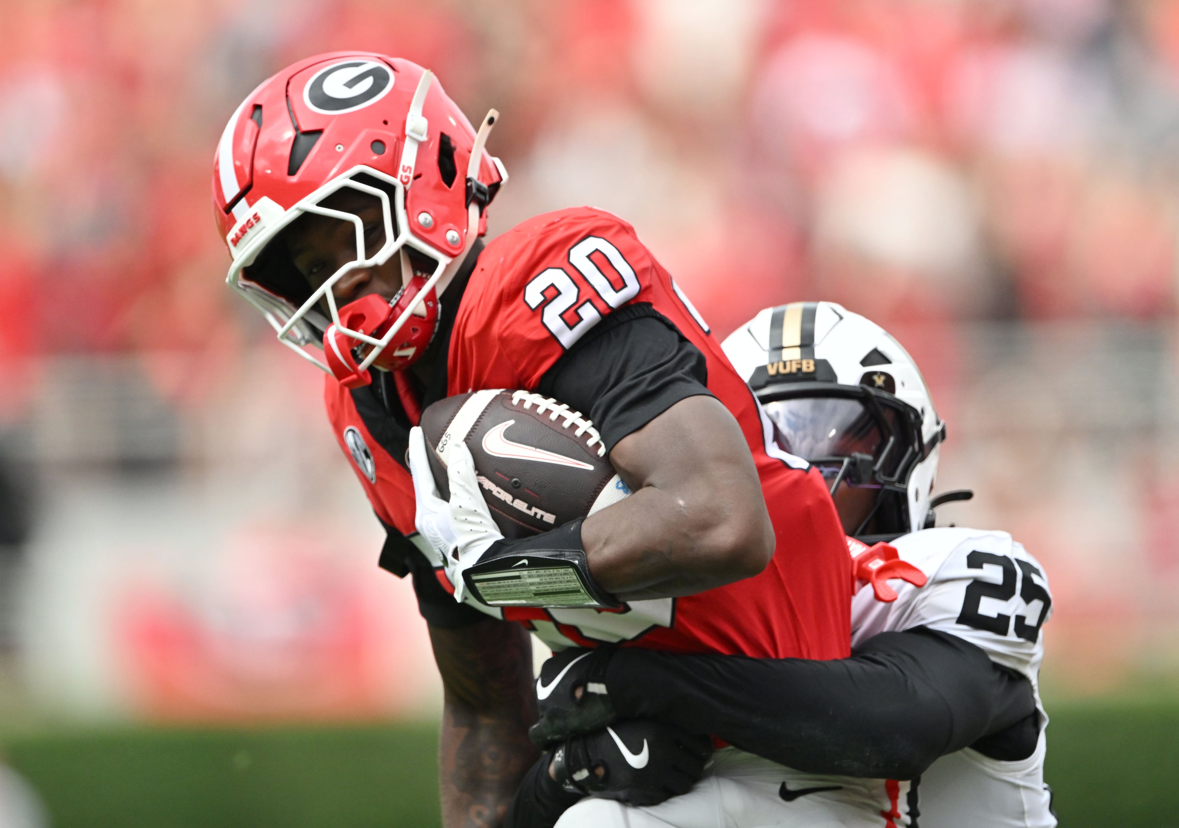 Georgia running back Dwight Phillips Jr. (20) runs as Vanderbilt safety Mason Lewis (25) tackles from behind during the first half in an NCAA football game at Sanford Stadium on Saturday, Oct. 3, 2026, in Athens. (Hyosub Shin/AJC)