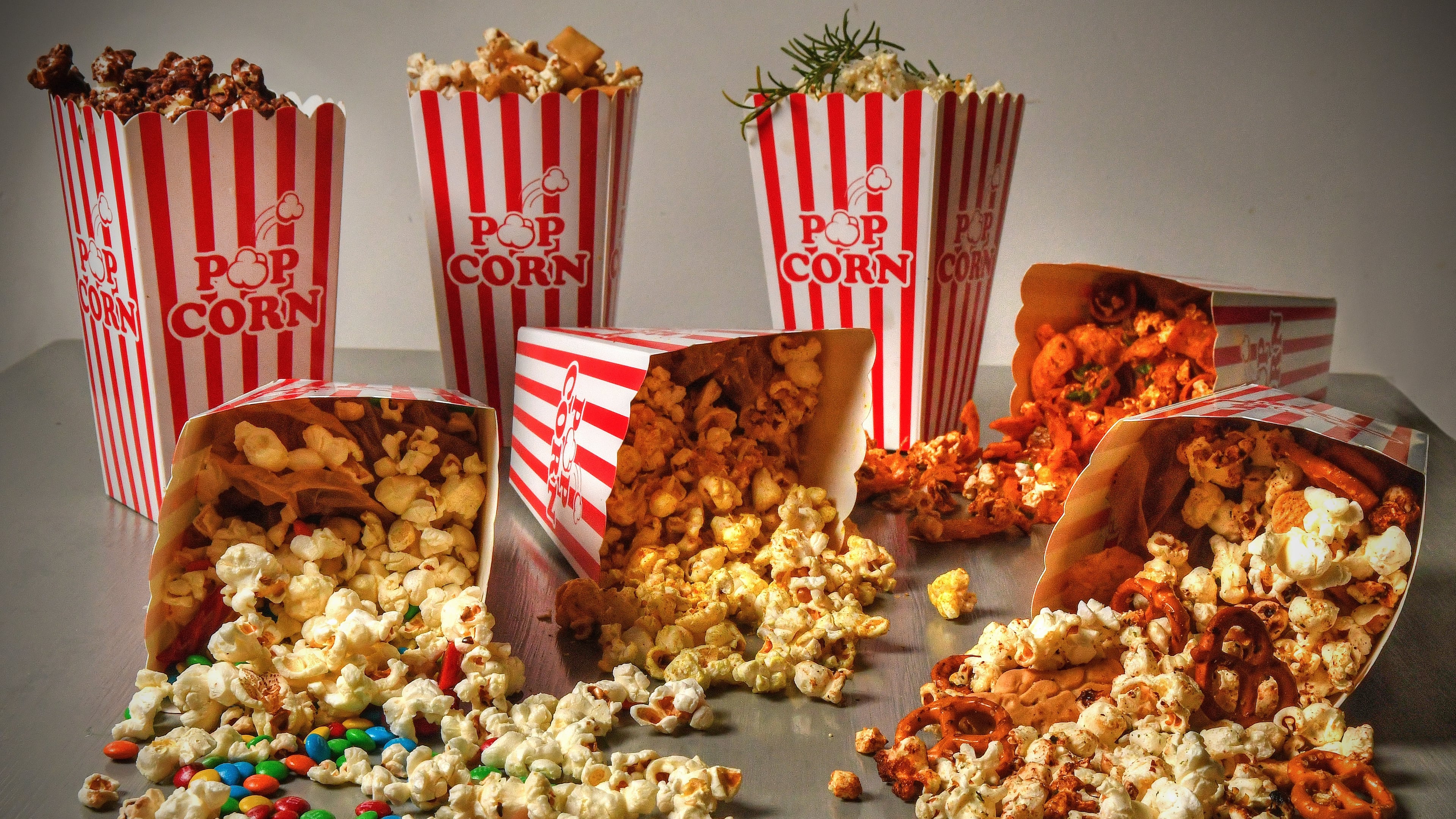 You have a choice of movies, so don't settle for plain old popcorn. Creative options include (back row from left) Dark Chocolate Sea Salt Popcorn, Sushi Popcorn, Olive Oil Popcorn with Garlic, Rosemary, and Parmesan; and (on their sides from left) Deluxe Movie Night Popcorn, Curry-Lime Popcorn, Frito Pie Popcorn and Hurricane Popcorn. (Styling by Susan Puckett / Chris Hunt for the AJC)