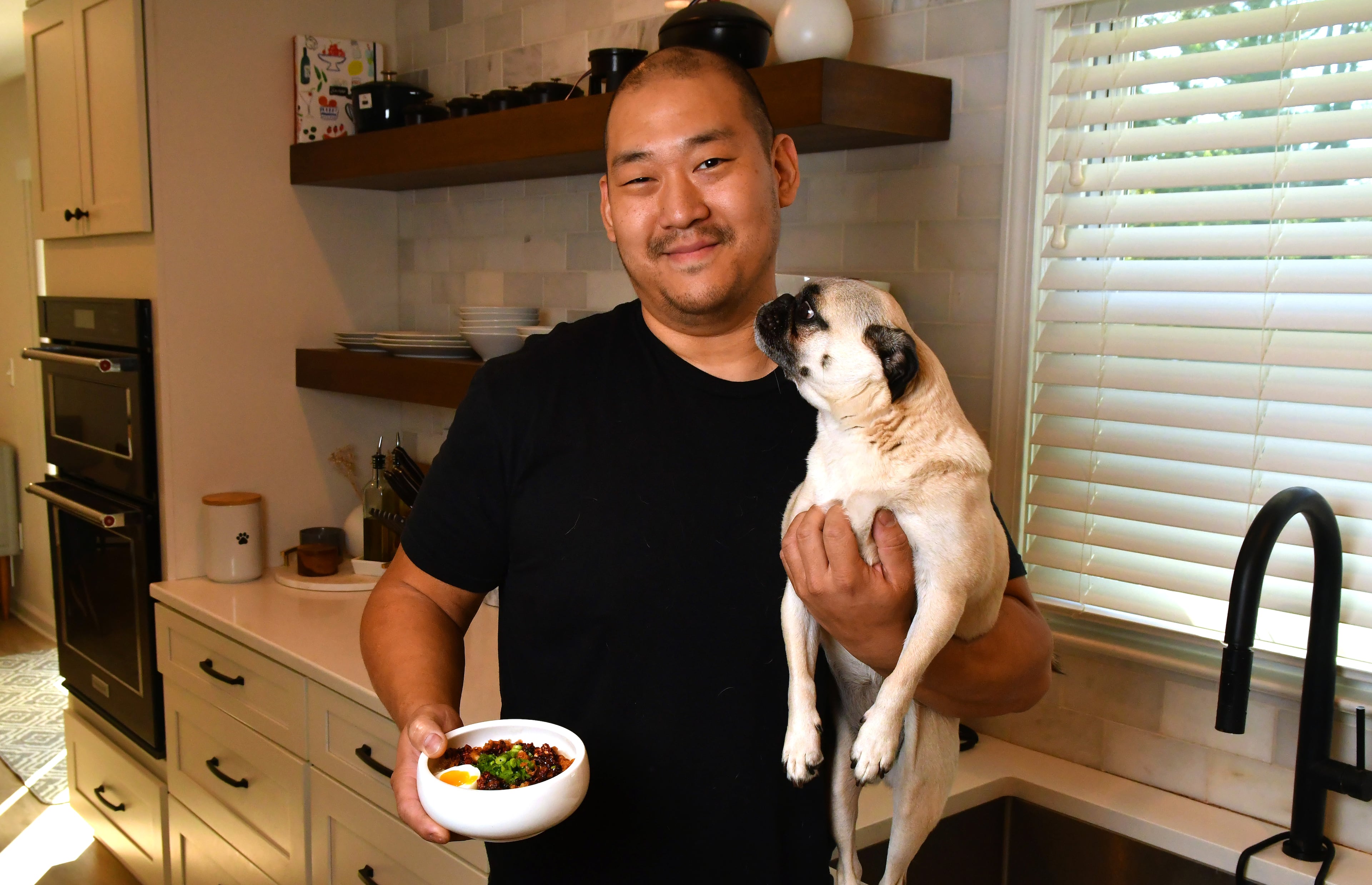 Chef Brian So stands in his Marietta home kitchen with one of his favorite pugs, Freddie. So says his fine-dining restaurant, Spring, quietly reopened in February. (Chris Hunt for the AJC 2023)