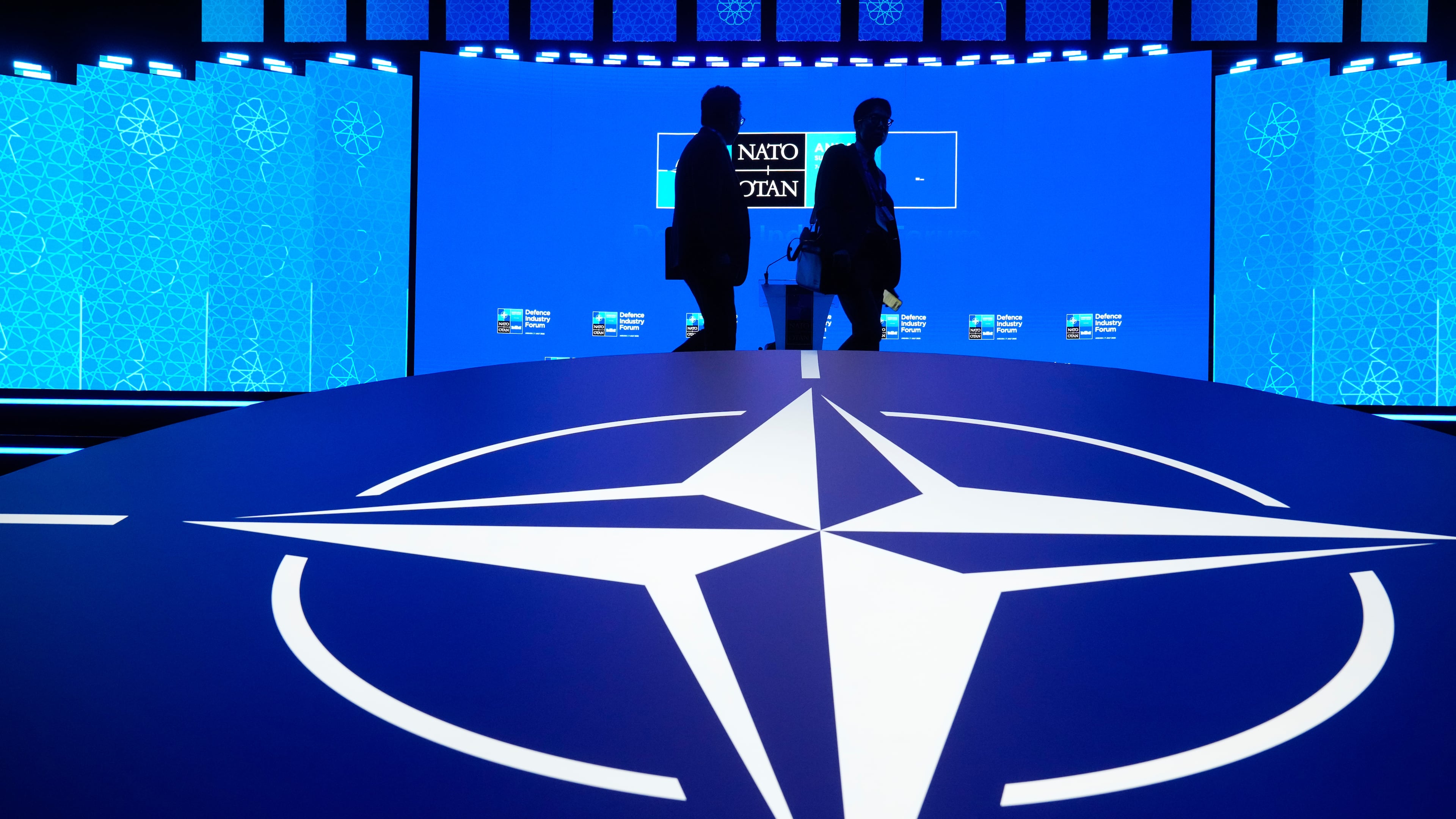 Two men walk past the NATO logo during the NATO Defense Industry Forum at the NATO summit in Ankara, Turkey, Tuesday, July 7, 2026. (AP Photo/Hussein Malla)