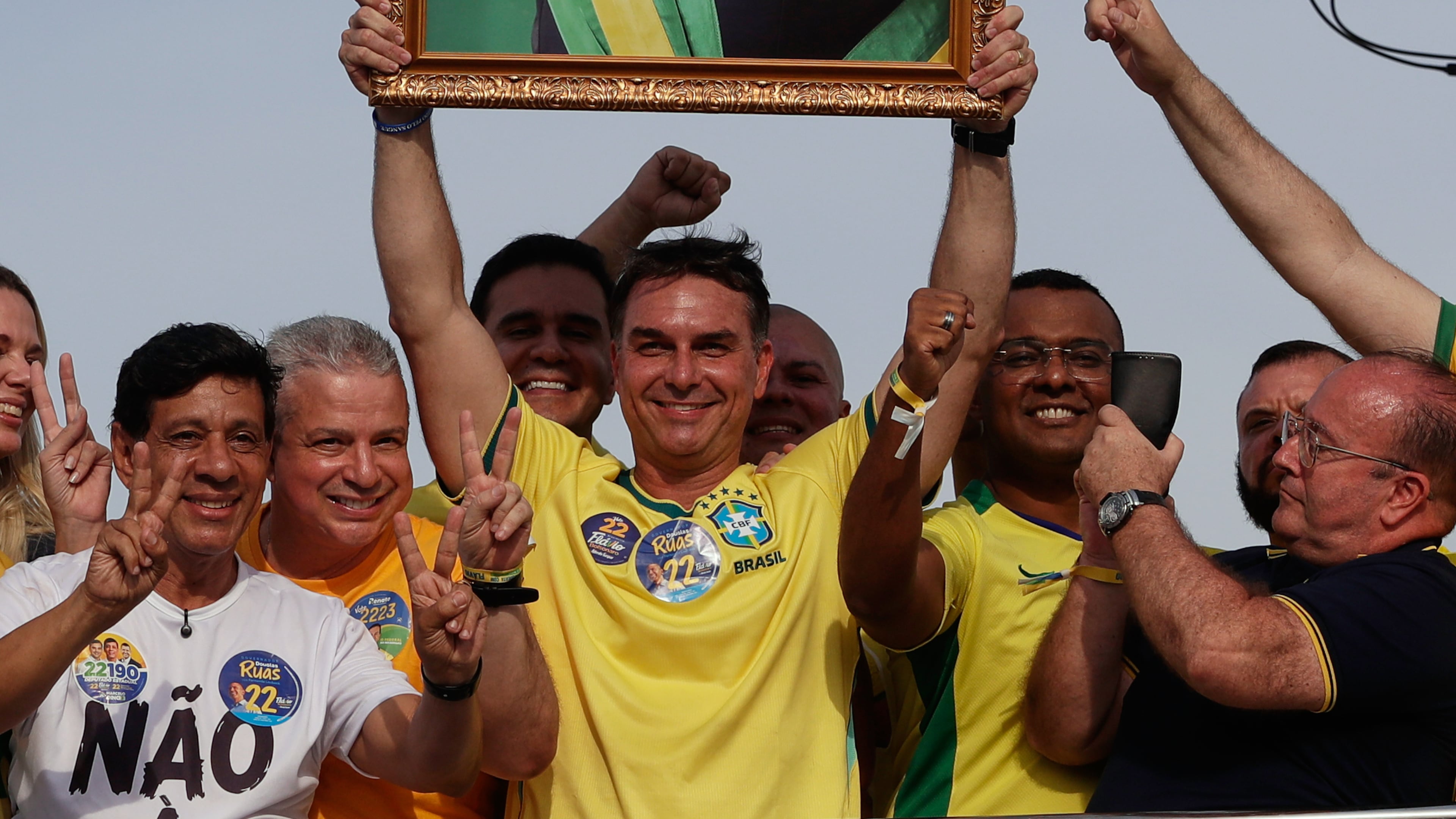 Opposition presidential candidate Flavio Bolsonaro holds a photo of his father, former President Jair Bolsonaro, as he rides a boat during a campaign rally ahead of the October general election in Angra dos Reis, Rio de Janeiro state, Brazil, Saturday, Aug. 29, 2026. (AP Photo/Bruna Prado)