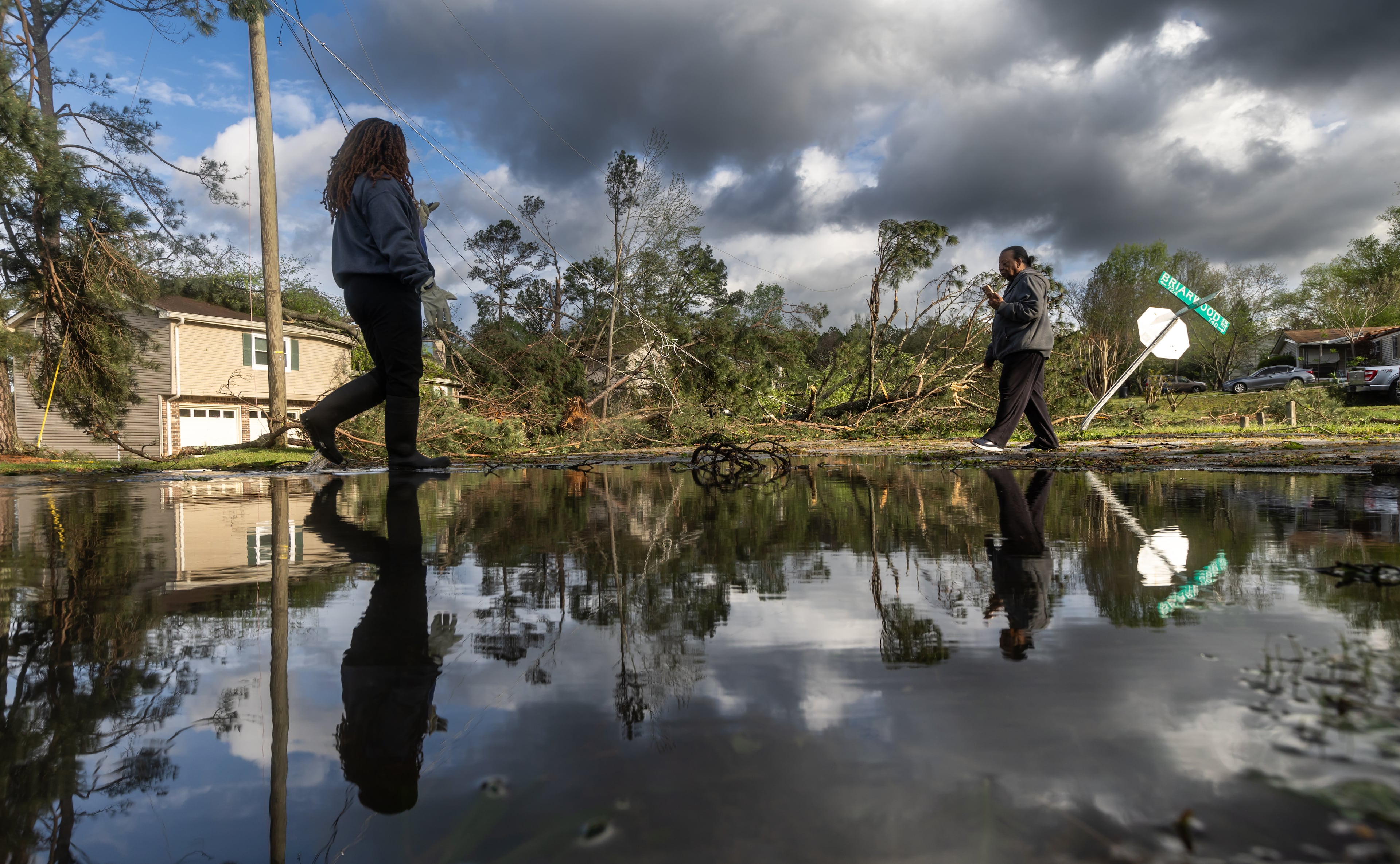 Where Briarwood Road and Briarwood Drive meet, Dianne Carter (left) and Brenda Gales (right) are reflected against the widespread damage after storms hit the area on the night of Tuesday, April 2, 2024 in Rockdale County. (John Spink / John.Spink@ajc.com)